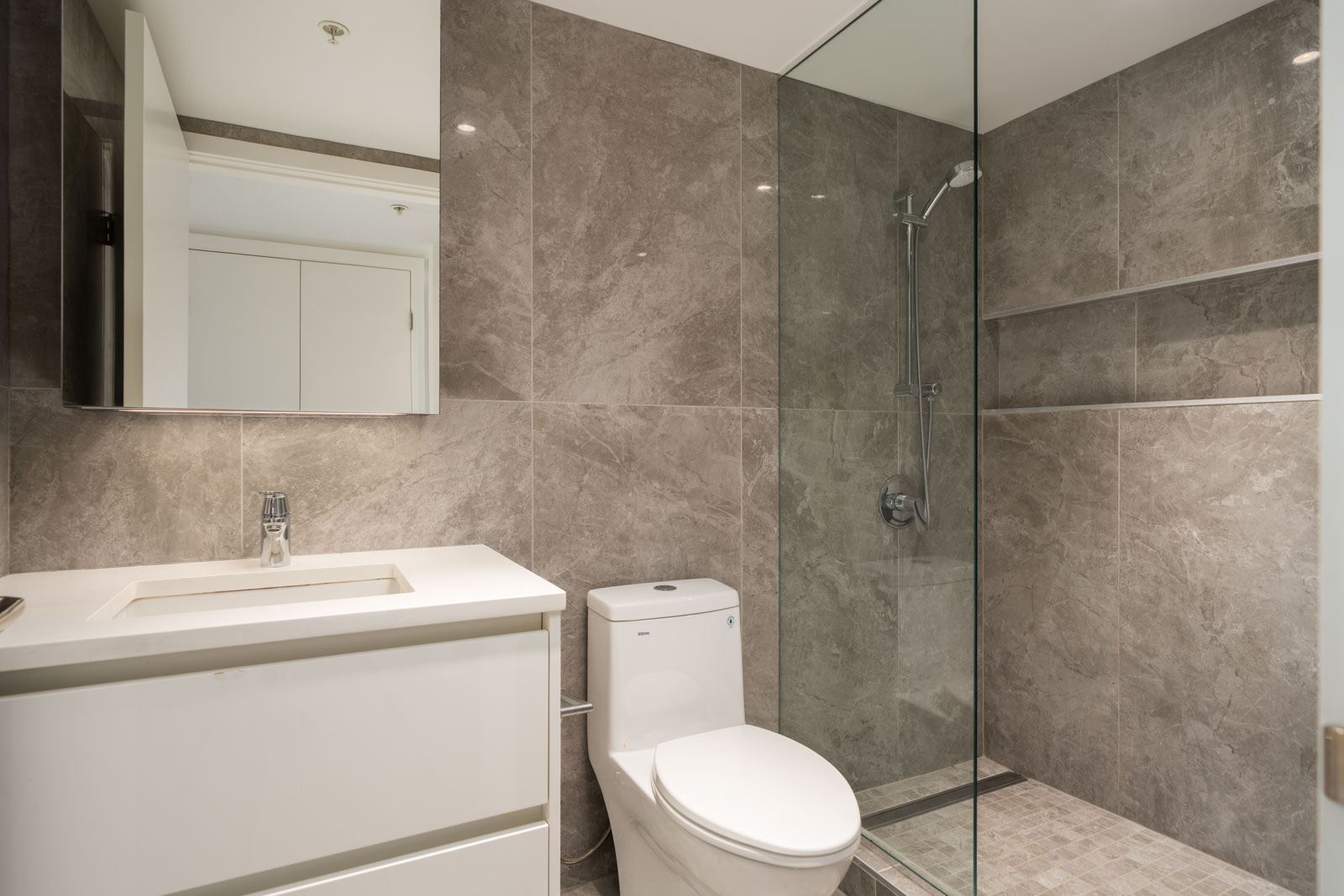 Modern bathroom at 6320 No.3 Rd, Richmond with a white vanity, toilet, and glass shower against gray tiled walls and floor.