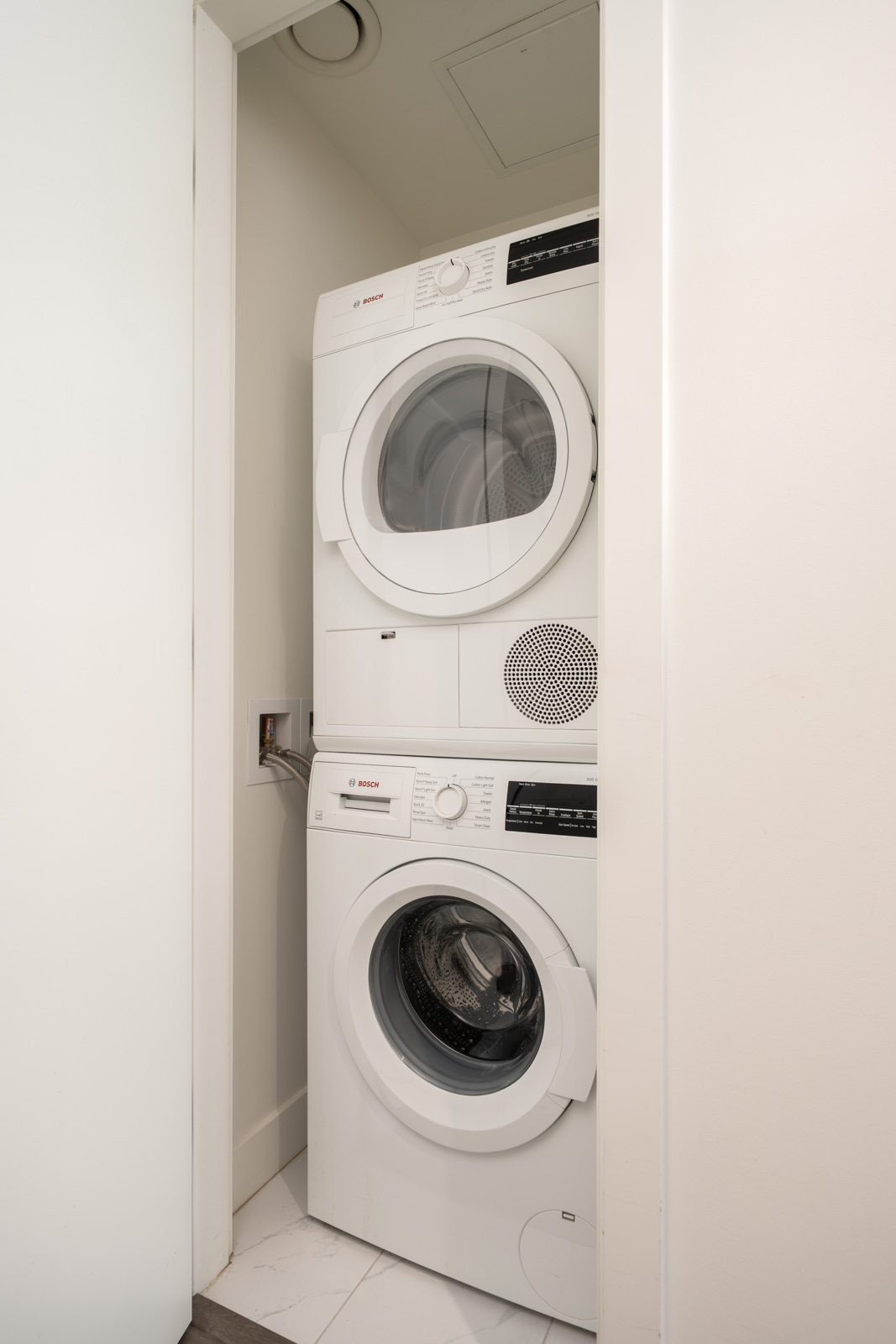 Stacked white Bosch washer and dryer in a compact laundry closet with a partially open door at 6320 No.3 Rd, Richmond.