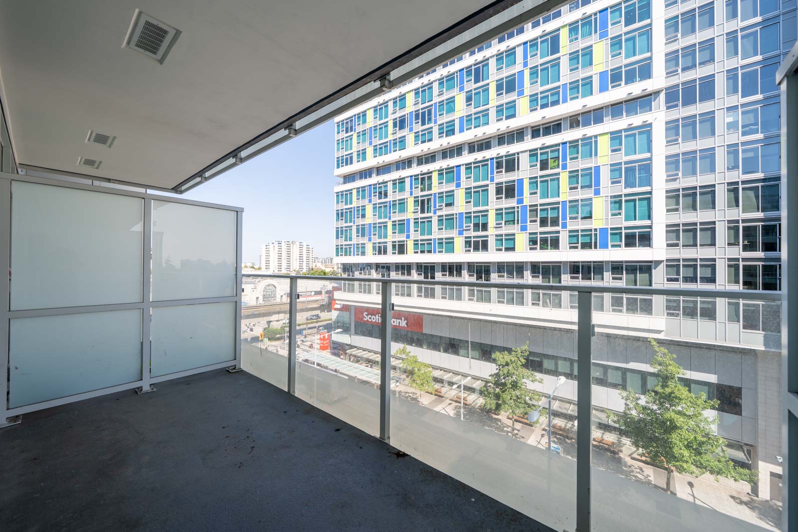 Empty balcony with glass railings overlooking a tree-lined street and office building in central Richmond, 6320 No.3 Rd.