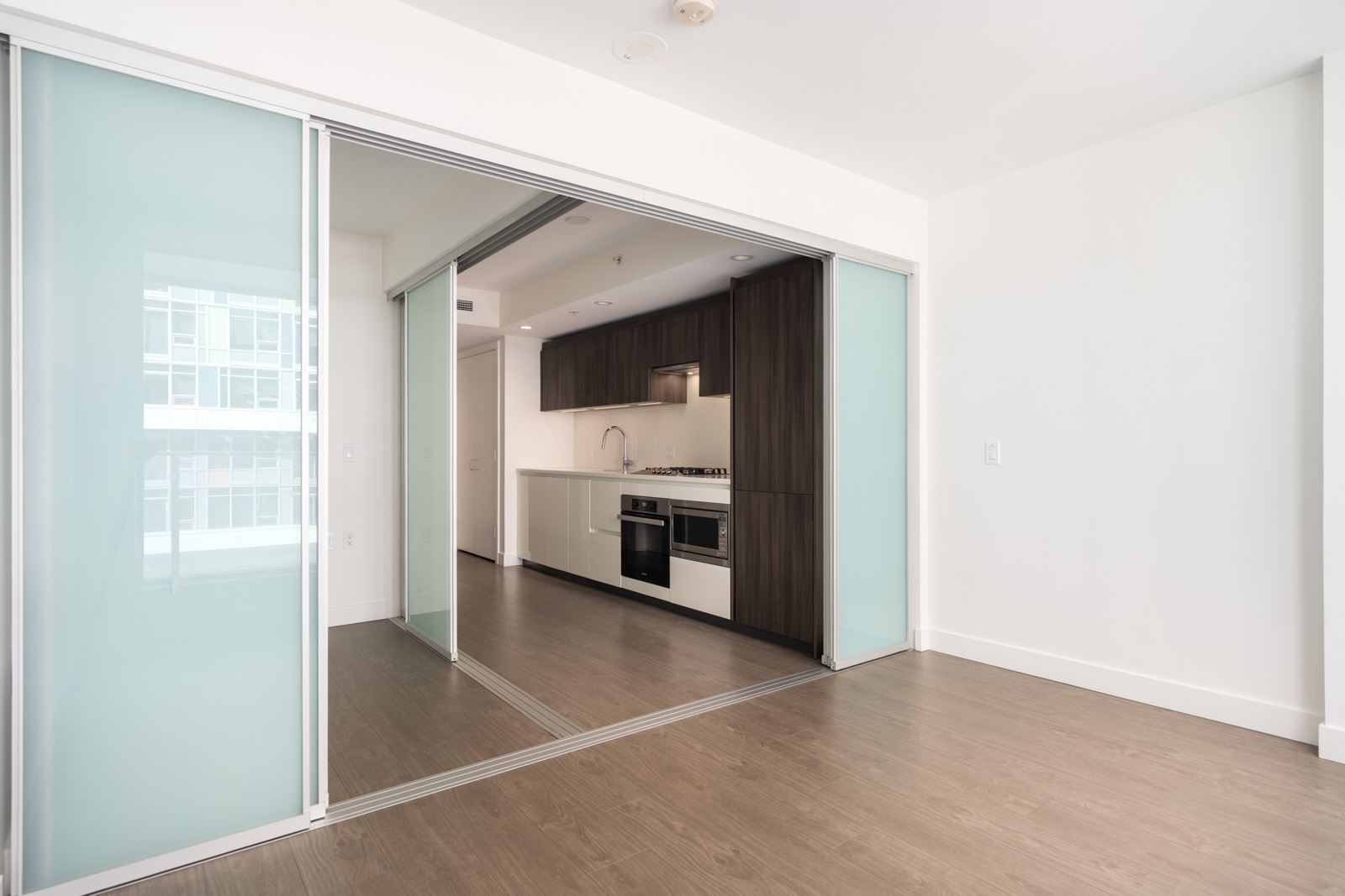 Modern kitchen with dark wood cabinets, white counters, stainless appliances, light wood floors, and frosted glass doors in Richmond.