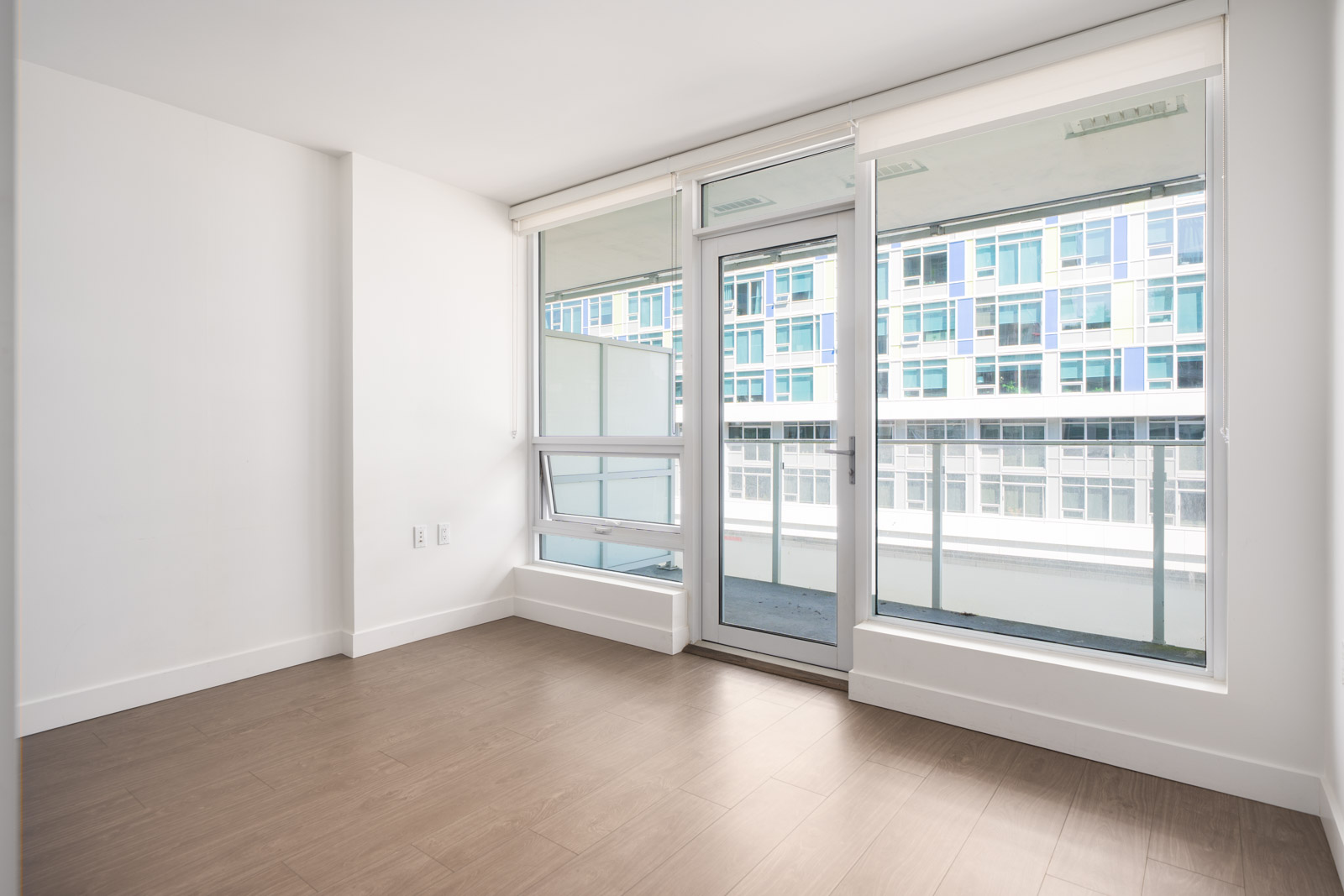 Empty room with light wood floors, white walls, and large windows opening to a balcony overlooking No.3 Rd, Richmond.