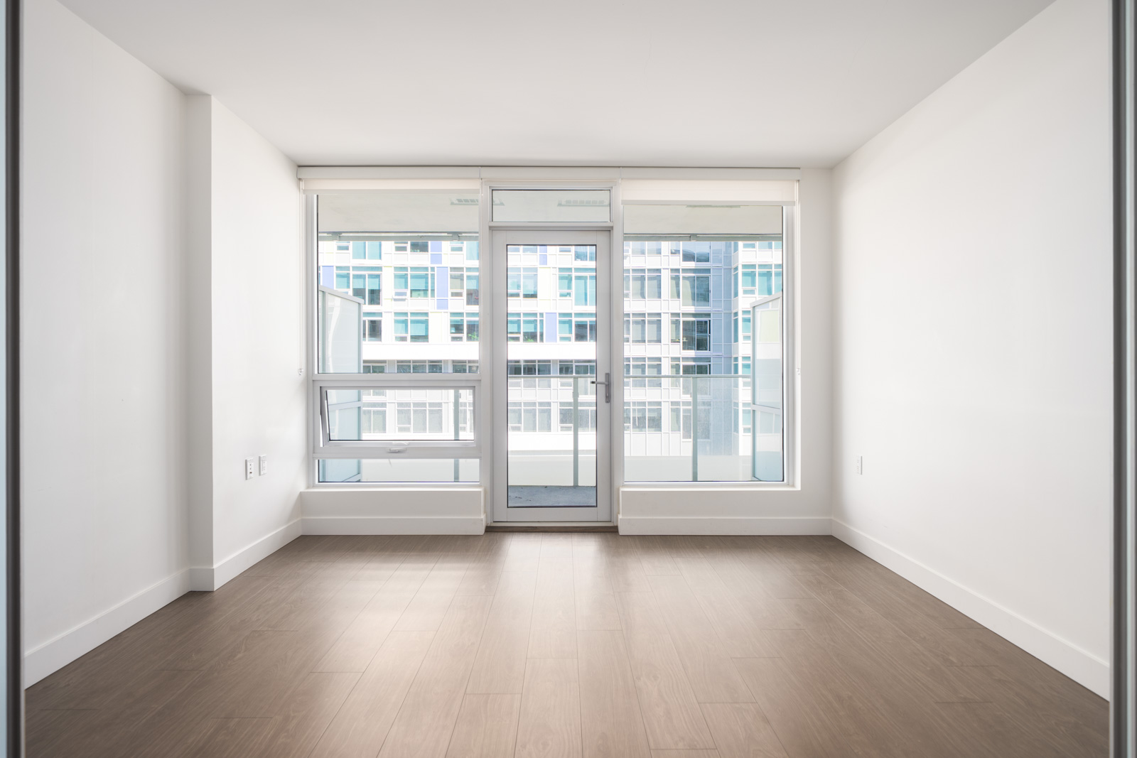 Empty, light-filled room on 6th floor at 6320 No.3 Rd, Richmond with pale walls, large windows, balcony door, and wood flooring.