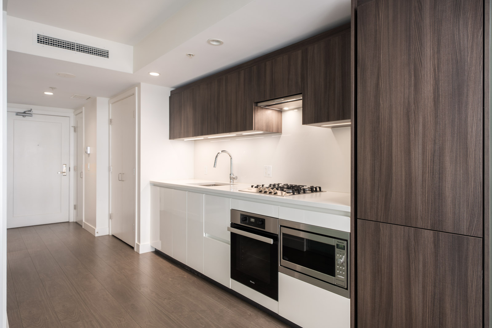 Modern kitchen at 6320 Richmond No.3 Rd with white cabinets, dark wood trim, built-in appliances, and overhead storage in a minimalist layout.