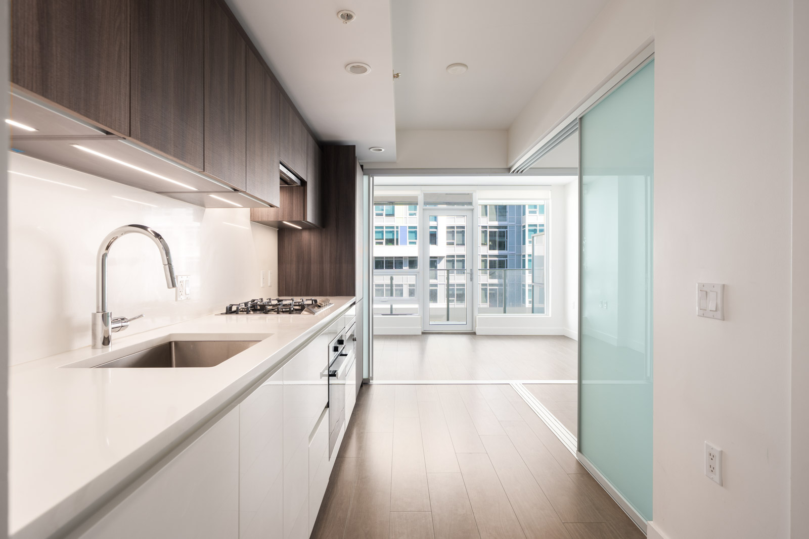 Modern kitchen with white countertops, built-in gas stove, wood cabinets, and sliding doors to a bright living area in Richmond.