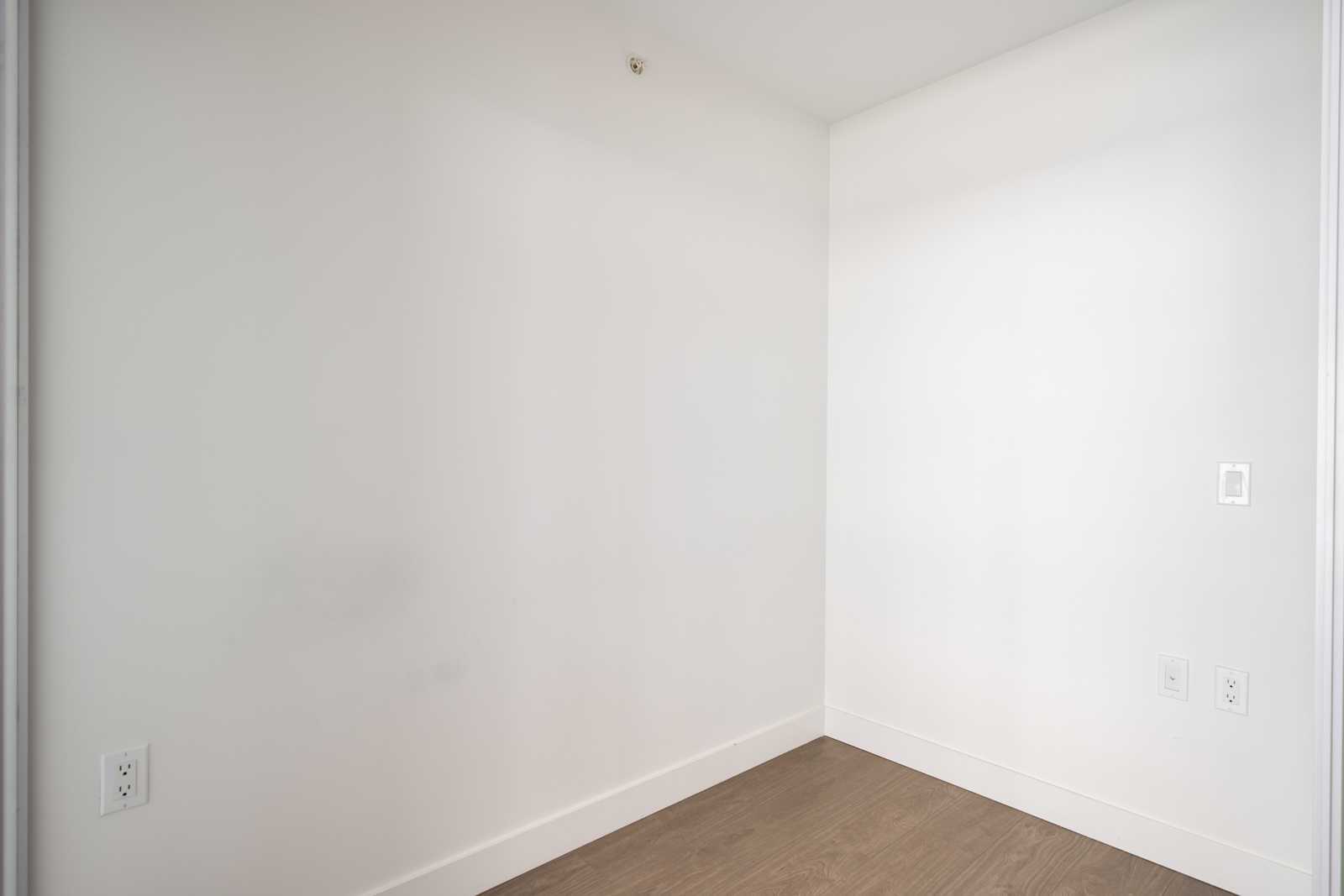 Empty corner of a room with white walls, light brown hardwood floor, and several electrical outlets at the baseboards in Richmond.