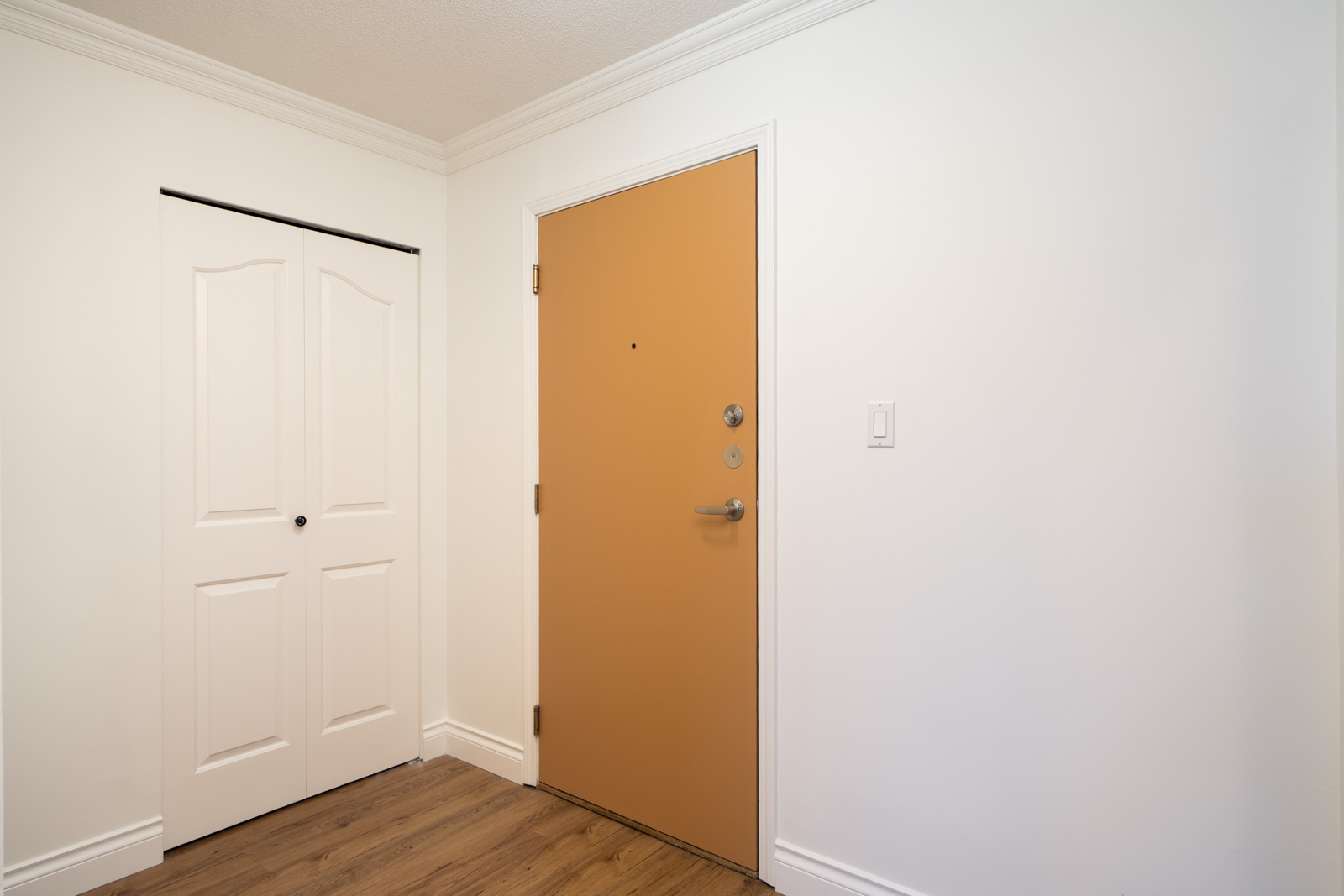 A light brown front door with silver hardware beside a white closet door in a white-walled, wood-floored room on Quayside Dr, New Westminster.