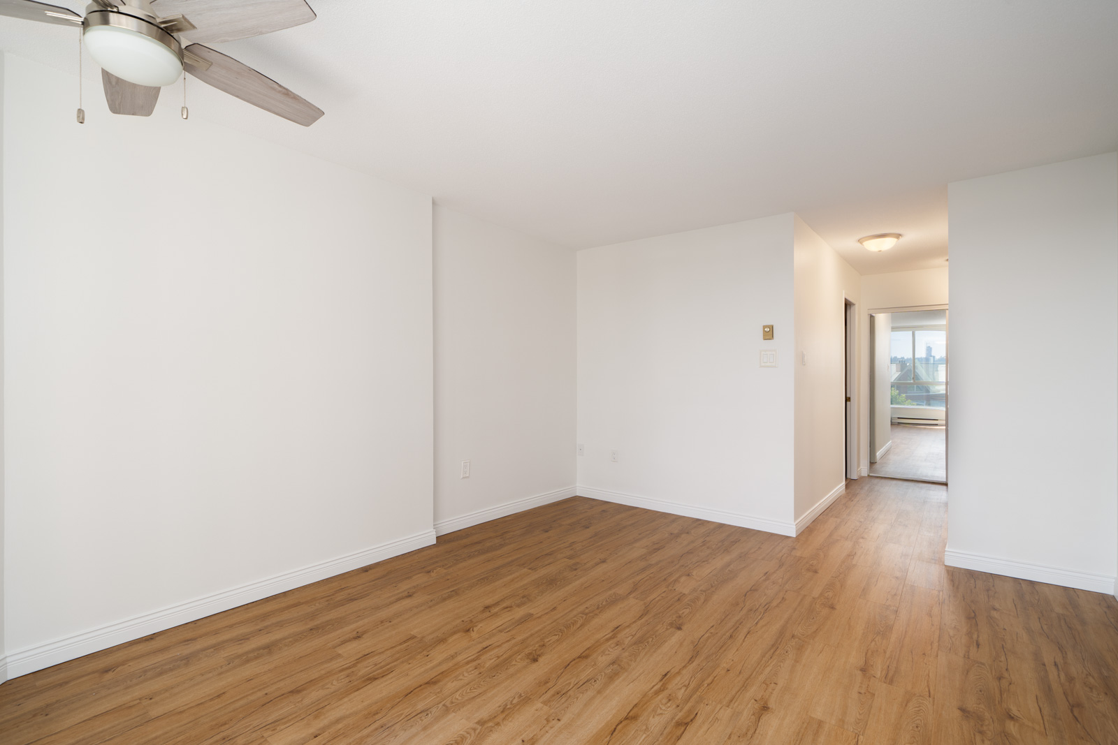 Unfurnished room with white walls, wood floors, ceiling fan, and hallway to a window on 12th floor, Quayside Dr, New Westminster.