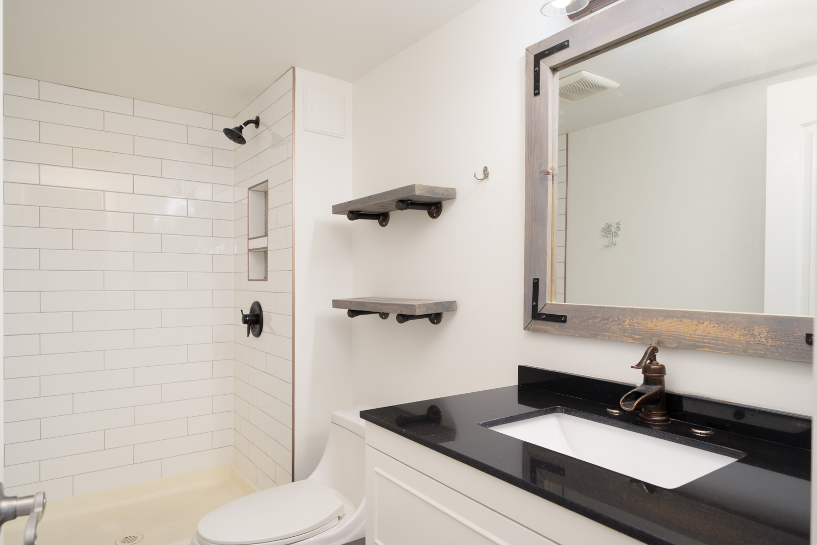 Modern New Westminster bathroom with black countertop sink, white cabinets, shelves, large mirror, and walk-in shower with black fixtures.