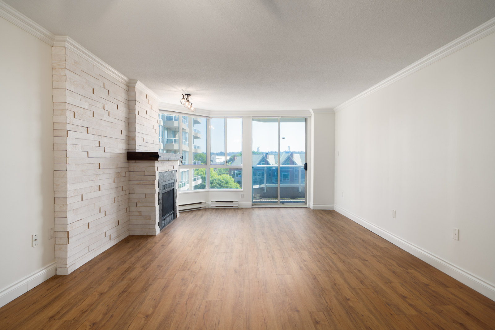 Empty living room with wood floors, white stone fireplace, and large windows facing buildings and trees. 12th floor, Quayside Dr, New Westminster.