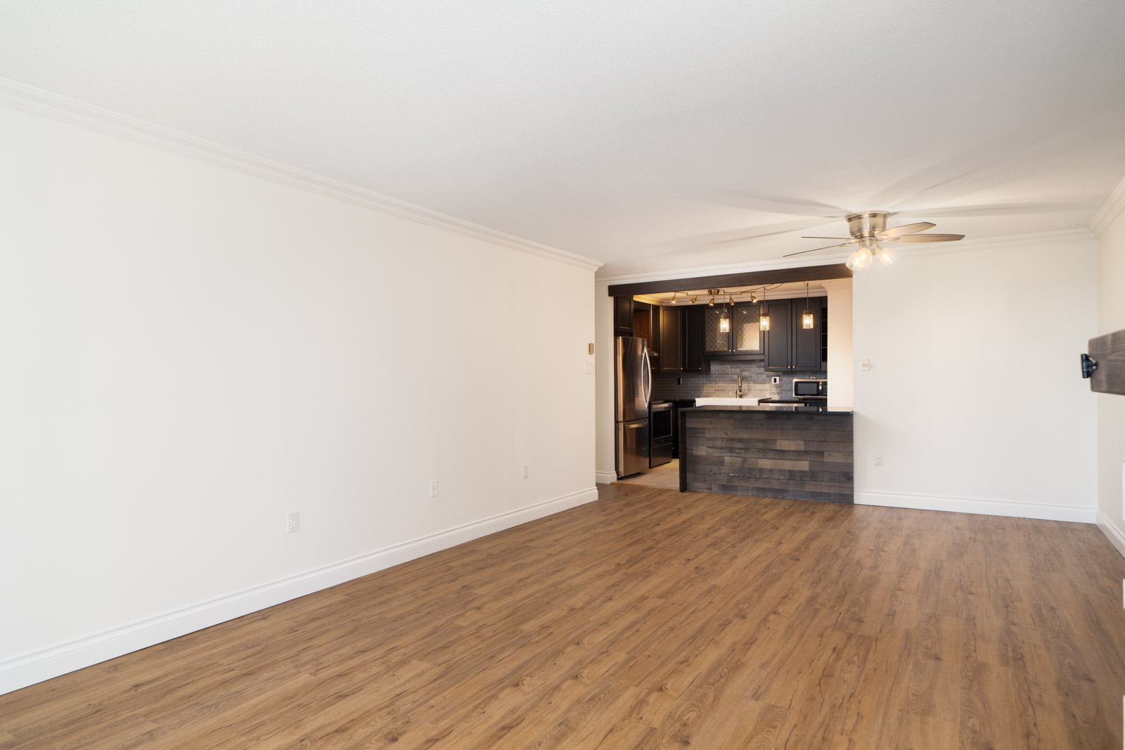 Unfurnished living room with wood floors, white walls, and open kitchen with dark cabinets. 12th floor, New Westminster.