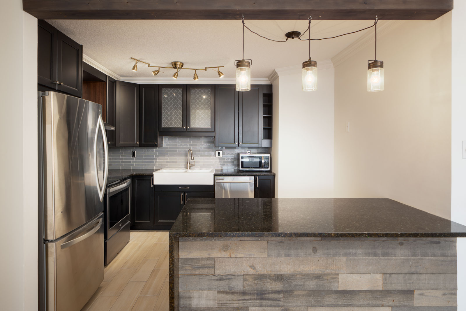 Modern kitchen with dark cabinets, stainless steel appliances, farmhouse sink, tile backsplash, and island on Quayside Dr., New Westminster.