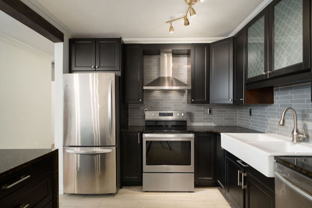 Modern kitchen at 1245 Quayside Dr, New Westminster with stainless appliances, black cabinets, farmhouse sink, and gray tile backsplash.