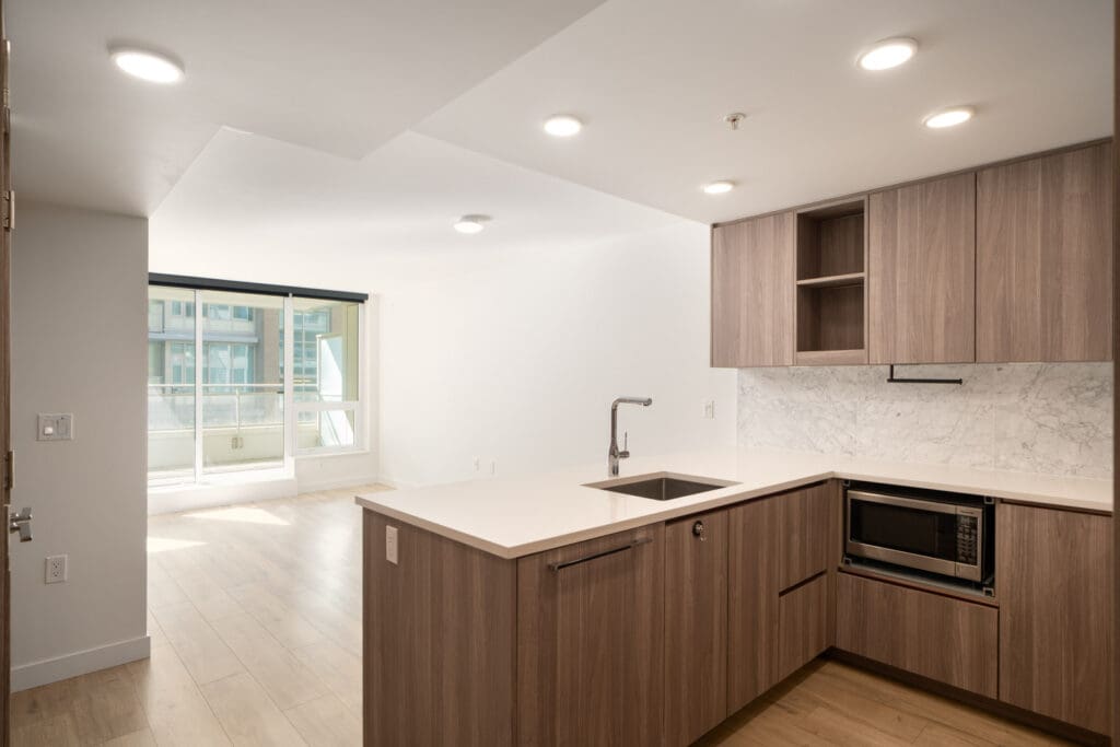 Modern Vancouver kitchen with wood cabinets, white counters, built-in microwave, and open layout facing bright living area with large windows.