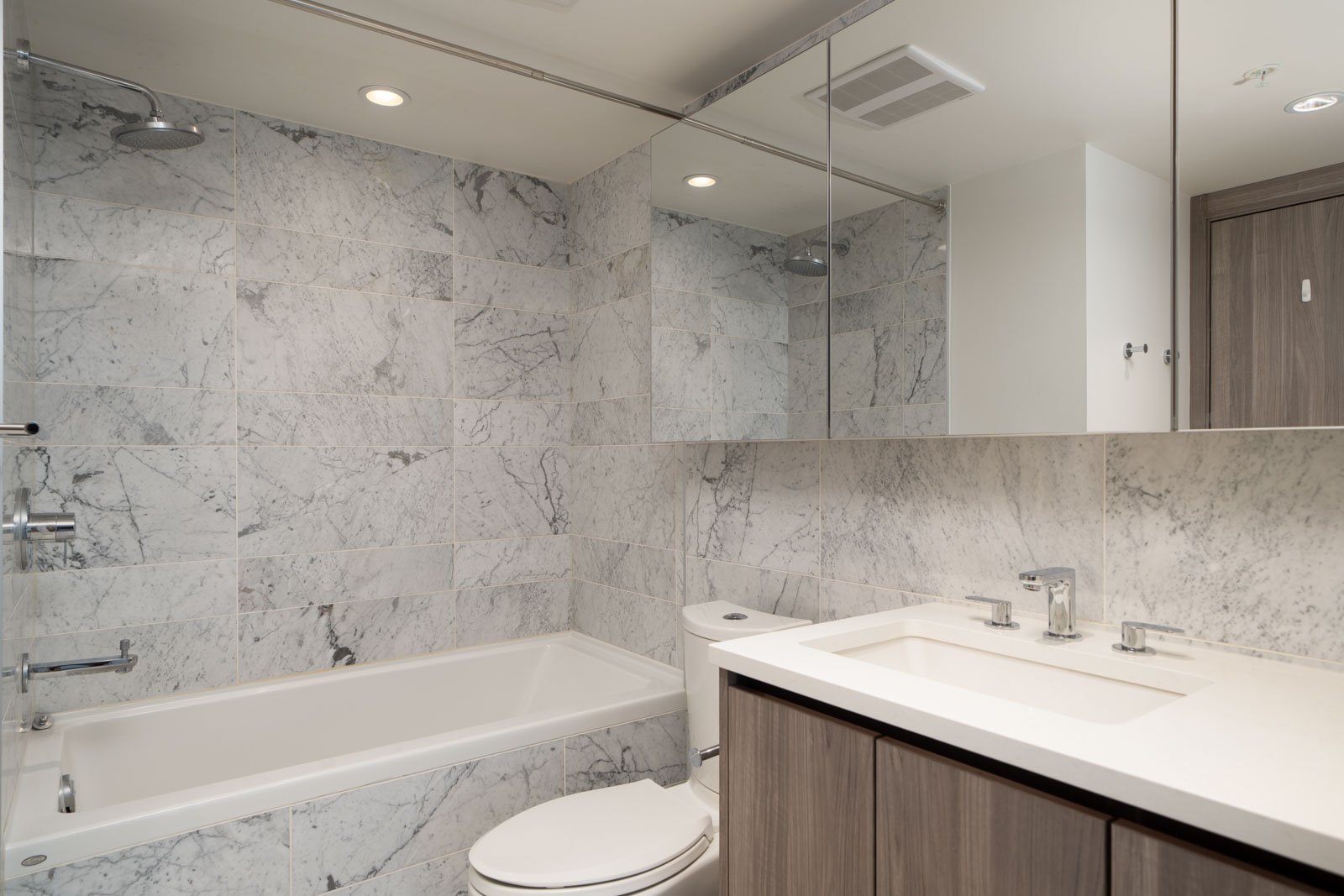 Modern bathroom on SW Marine Dr, Vancouver featuring marble tile walls, tub-shower combo, toilet, large mirror, and wood vanity.