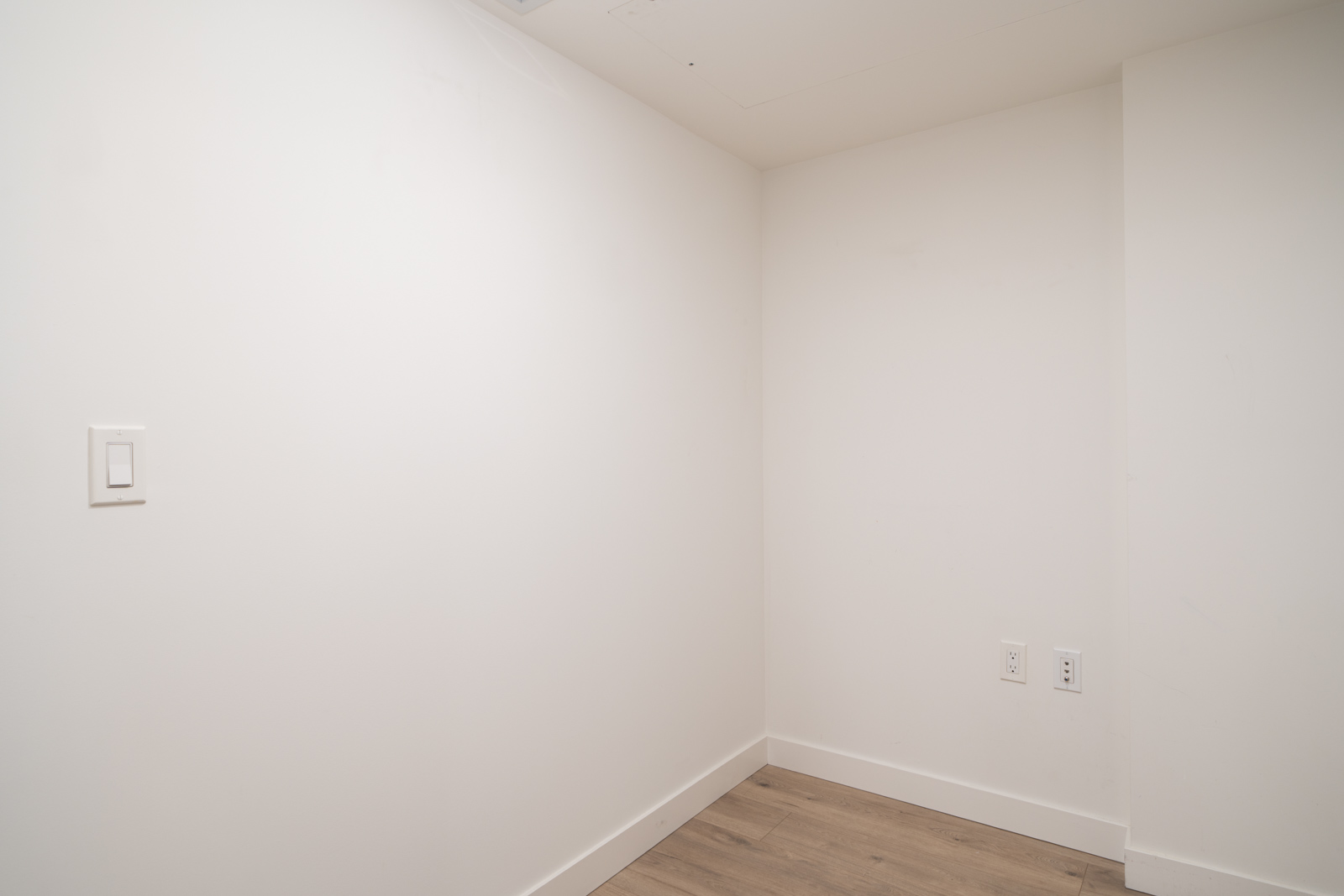 White corner of a room at 455 SW Marine, Vancouver, with light wood floors, a left wall light switch, and two right wall outlets.