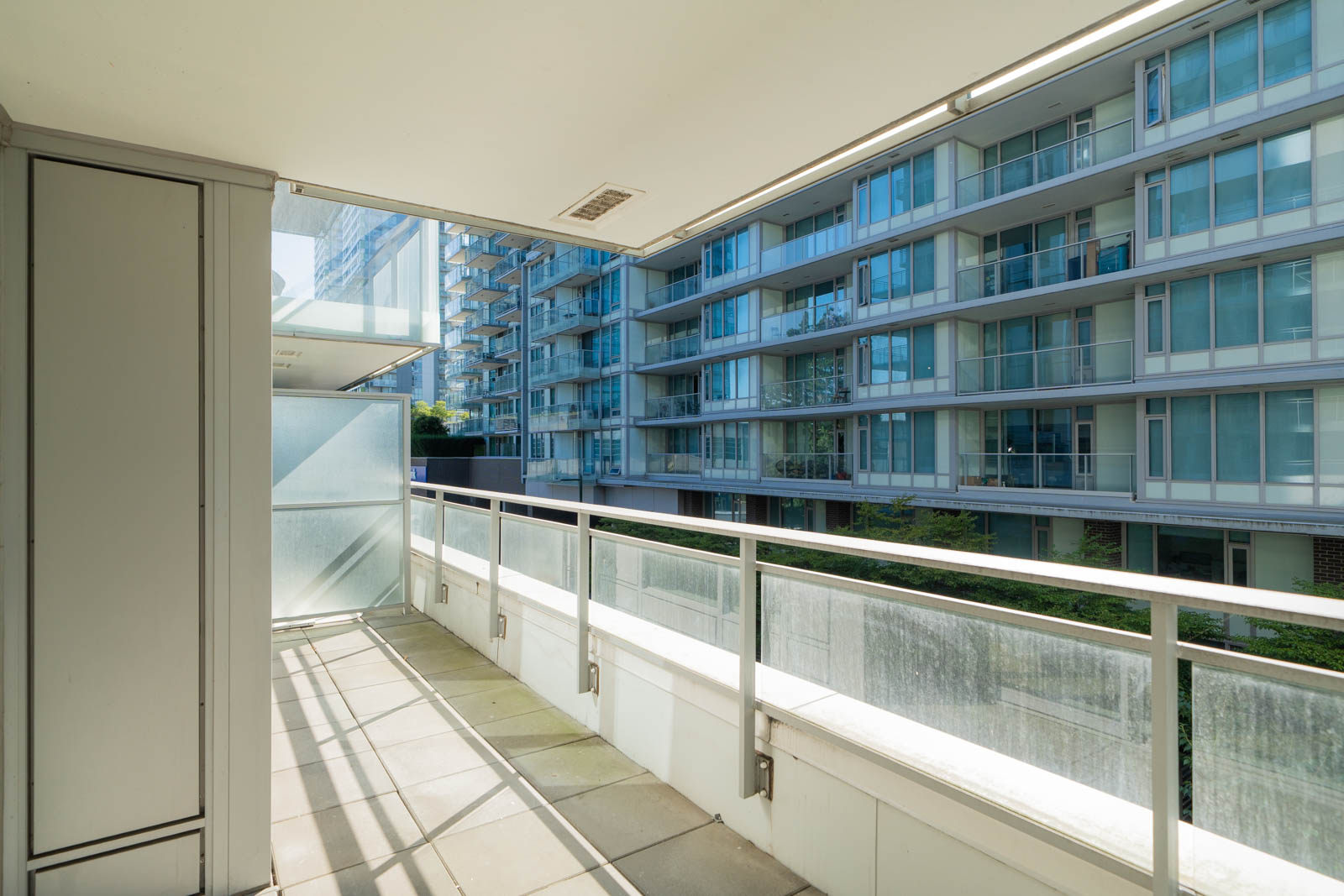 Balcony with glass railing and tiled floor overlooking glass-walled buildings in bright daylight at 455 SW Marine Dr, Vancouver.