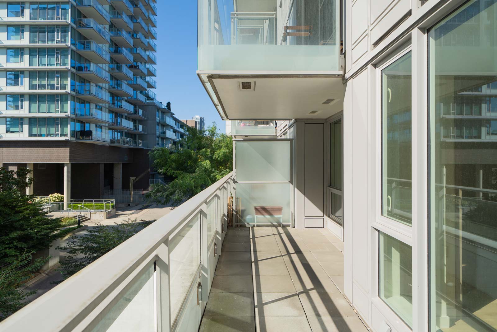 Sunny balcony of a modern SW Marine Dr apartment in Vancouver with glass railings, light tiles, and views of buildings and trees.