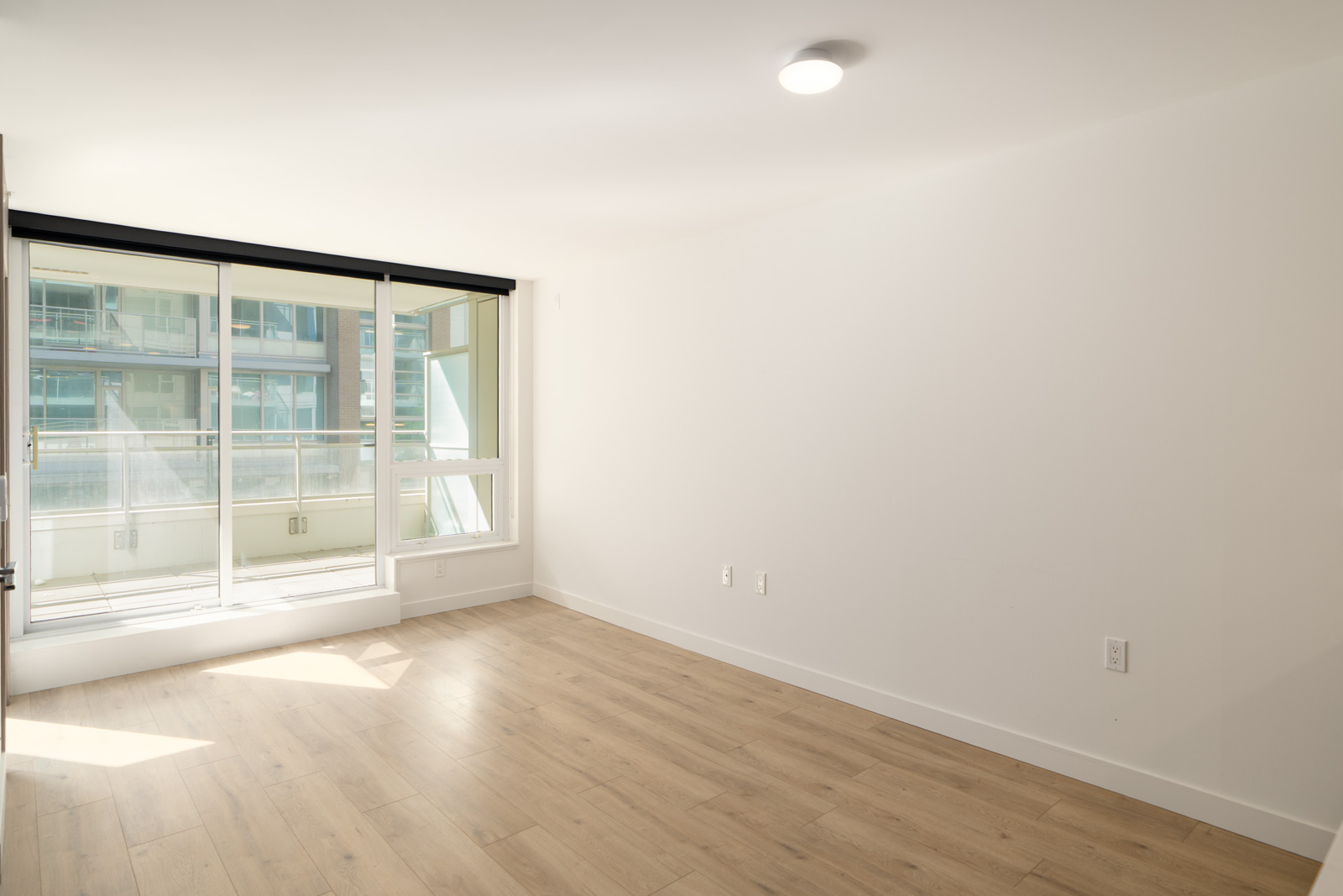 Empty room on SW Marine Dr, Vancouver with light wood floors, white walls, large windows, and a sliding door to a bright balcony.