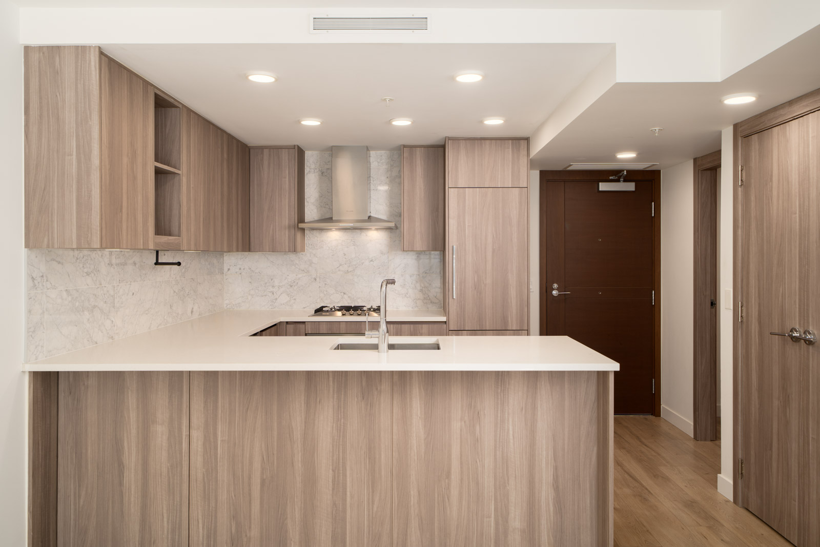 Modern kitchen in Vancouver’s SW Marine Dr area with light wood cabinets, marble backsplash, and a brown entry door in back.