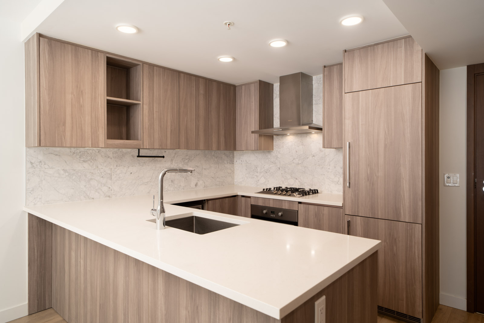 Modern kitchen in Vancouver with wood cabinets, marble backsplash, built-in oven, gas cooktop, and large island under recessed lights.