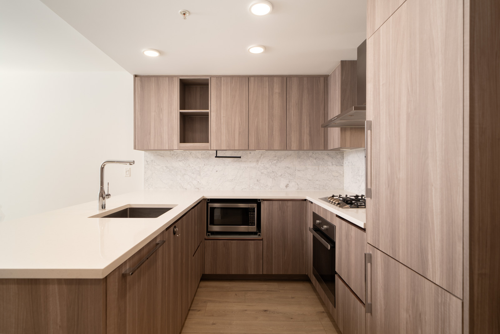 Modern Vancouver kitchen with light wood cabinets, built-in appliances, white counters, and a marble backsplash under recessed lighting.