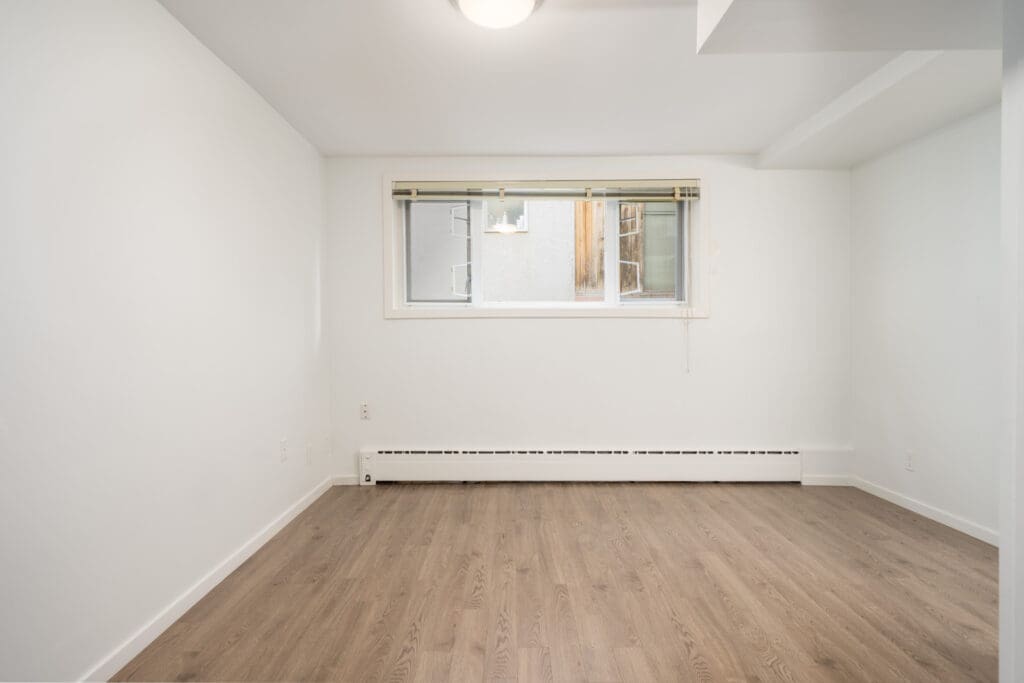 Unfurnished room with white walls, large window with blinds, ceiling light, baseboard heater, and wood-look floor in Vancouver.