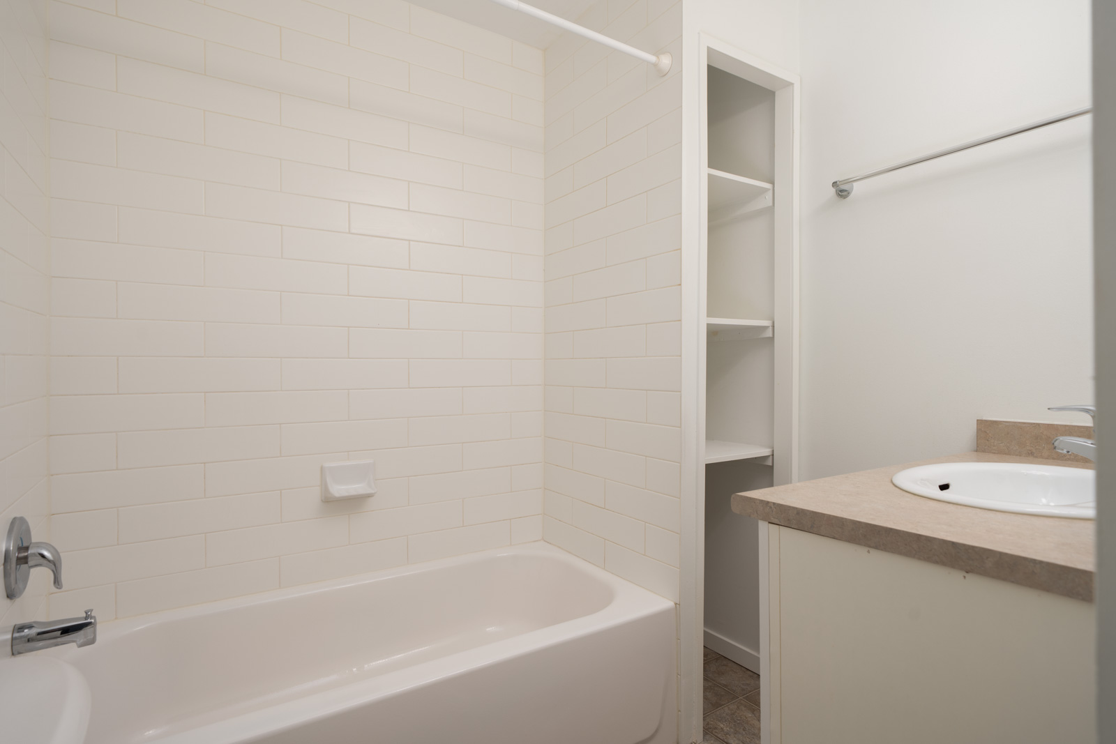 Lower floor bathroom at 1445 W 11th Ave, Vancouver with white tub, tiled walls, open shelves, towel bar, and sink on beige counter.