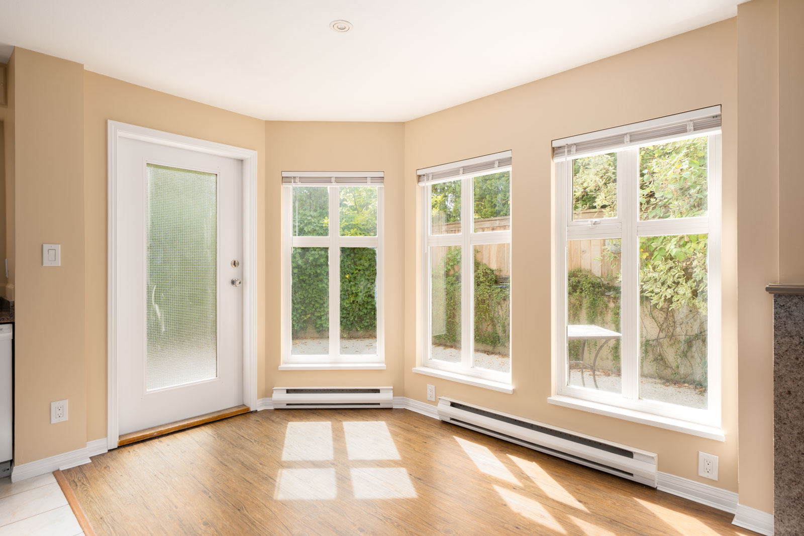 Bright, empty room with beige walls, large windows, wood floors, and a frosted glass door on the 1st floor in Vancouver.