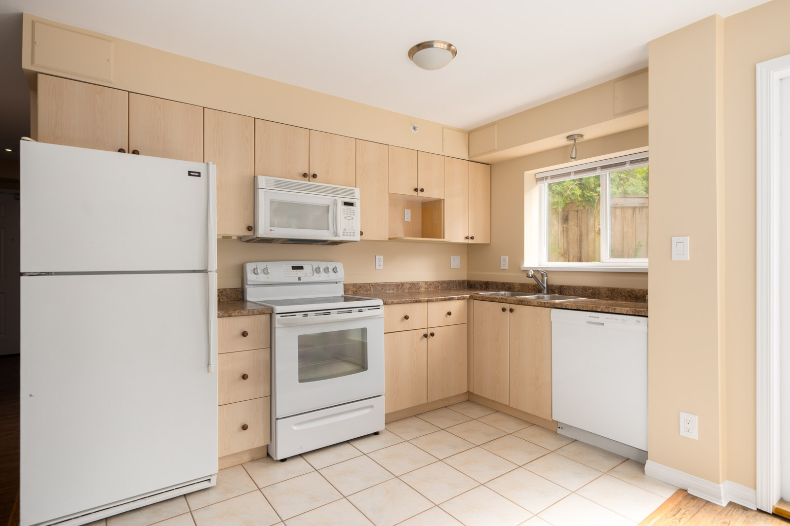 Modern first-floor kitchen at 1099 West 71st Ave, Vancouver, with light wood cabinets, white appliances, and a window over the sink.