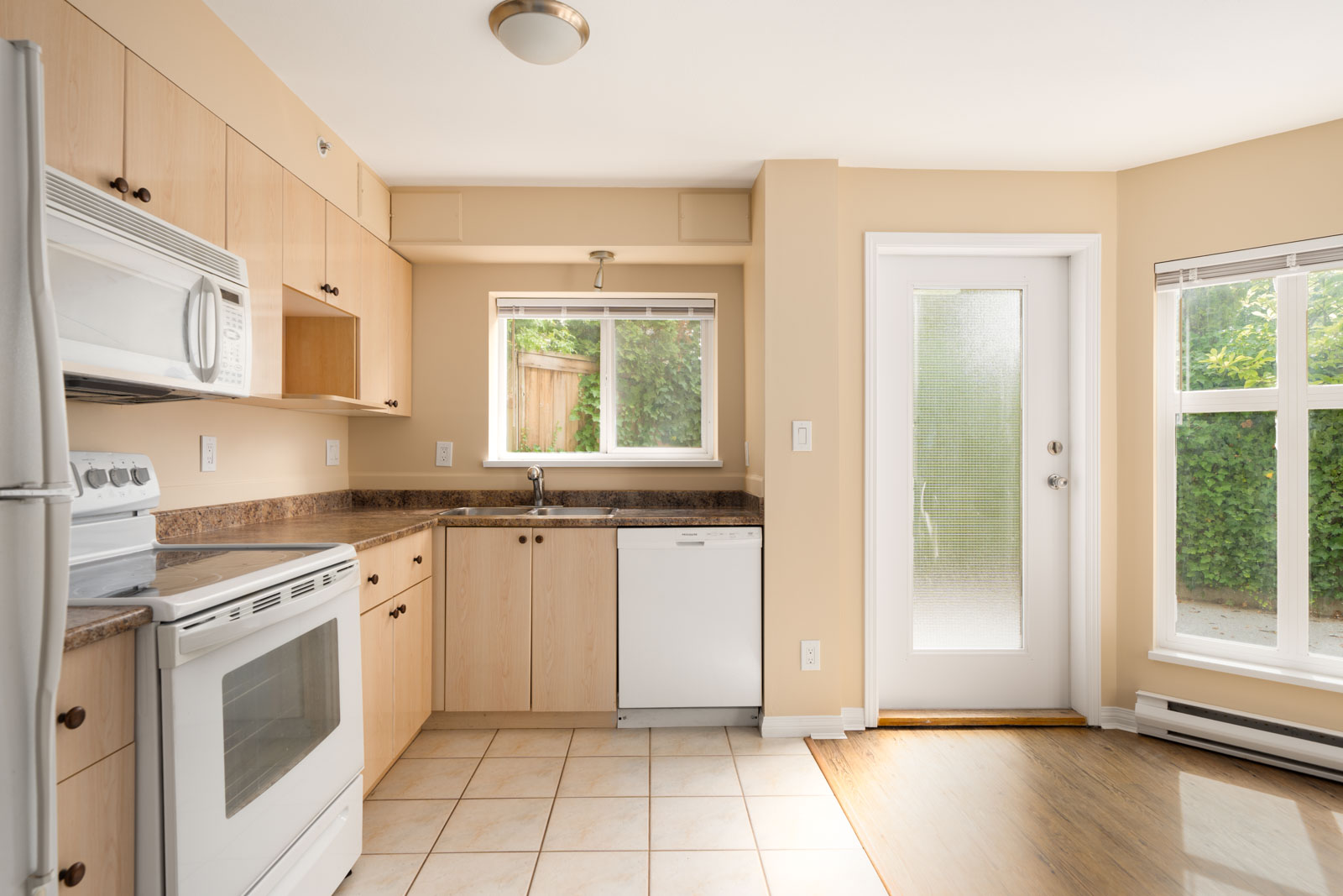 Compact kitchen on first floor at 1099 West 71st Ave, Vancouver with light wood cabinets, white appliances, tile floor, and large windows.