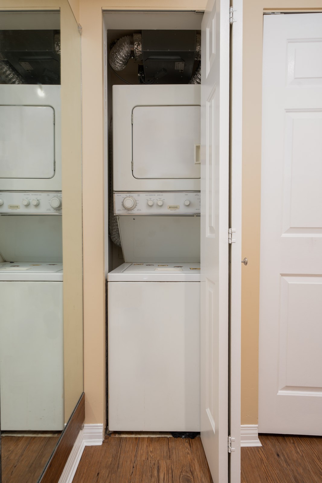 Stacked washer and dryer in a small laundry closet with a partially open door, next to a mirror on the 1st floor in Vancouver.