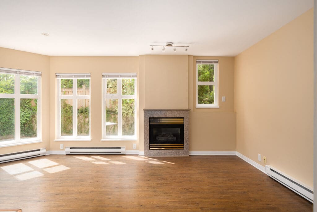 Unfurnished living room in Vancouver with light tan walls, wood floor, large windows, and a fireplace under a small window.