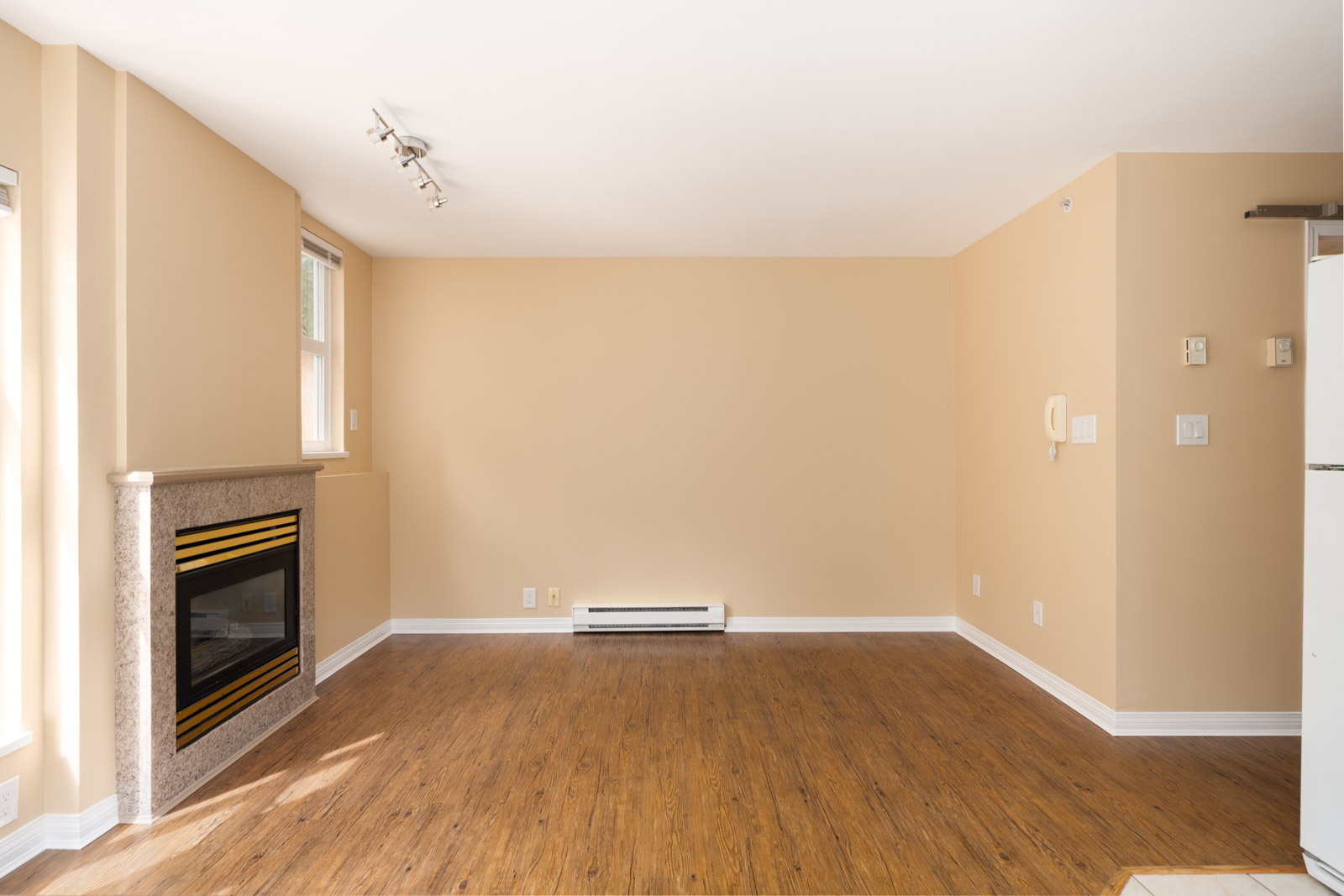Unfurnished 1st-floor room at 1099 West 71st Ave, Vancouver, with light beige walls, wood floors, fireplace, and fridge in view.
