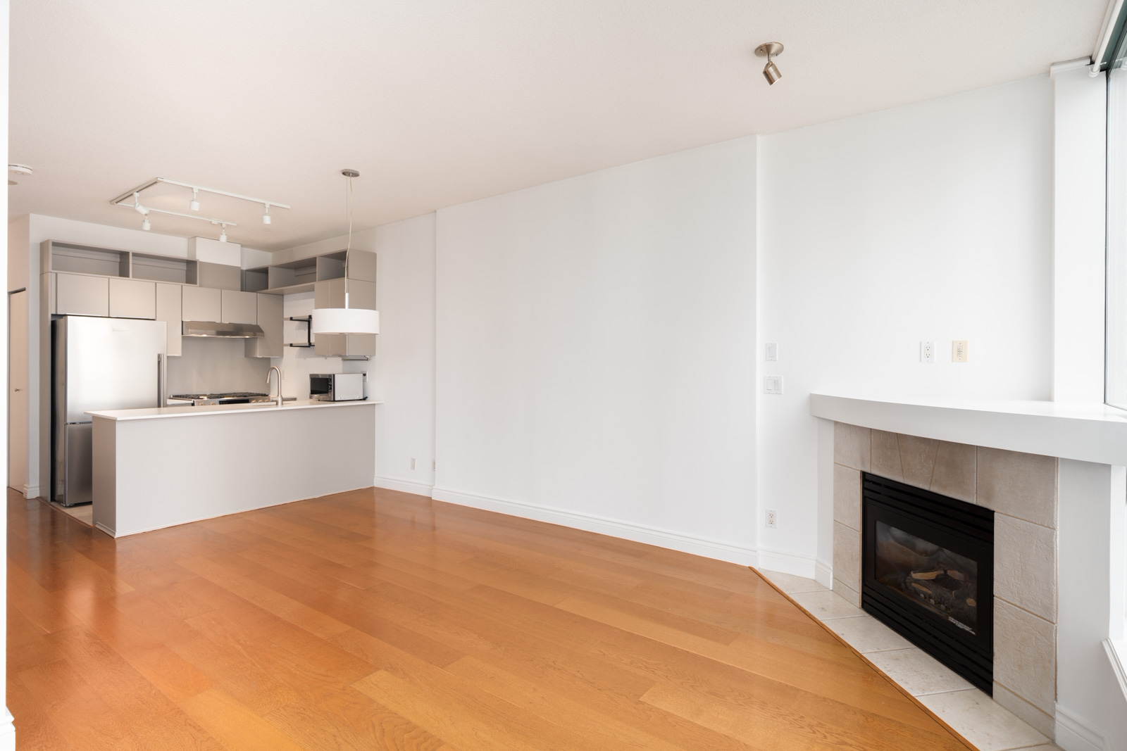 Unfurnished apartment at 1239 W Georgia St, Vancouver, with hardwood floors, modern kitchen, white walls, large windows, and fireplace.