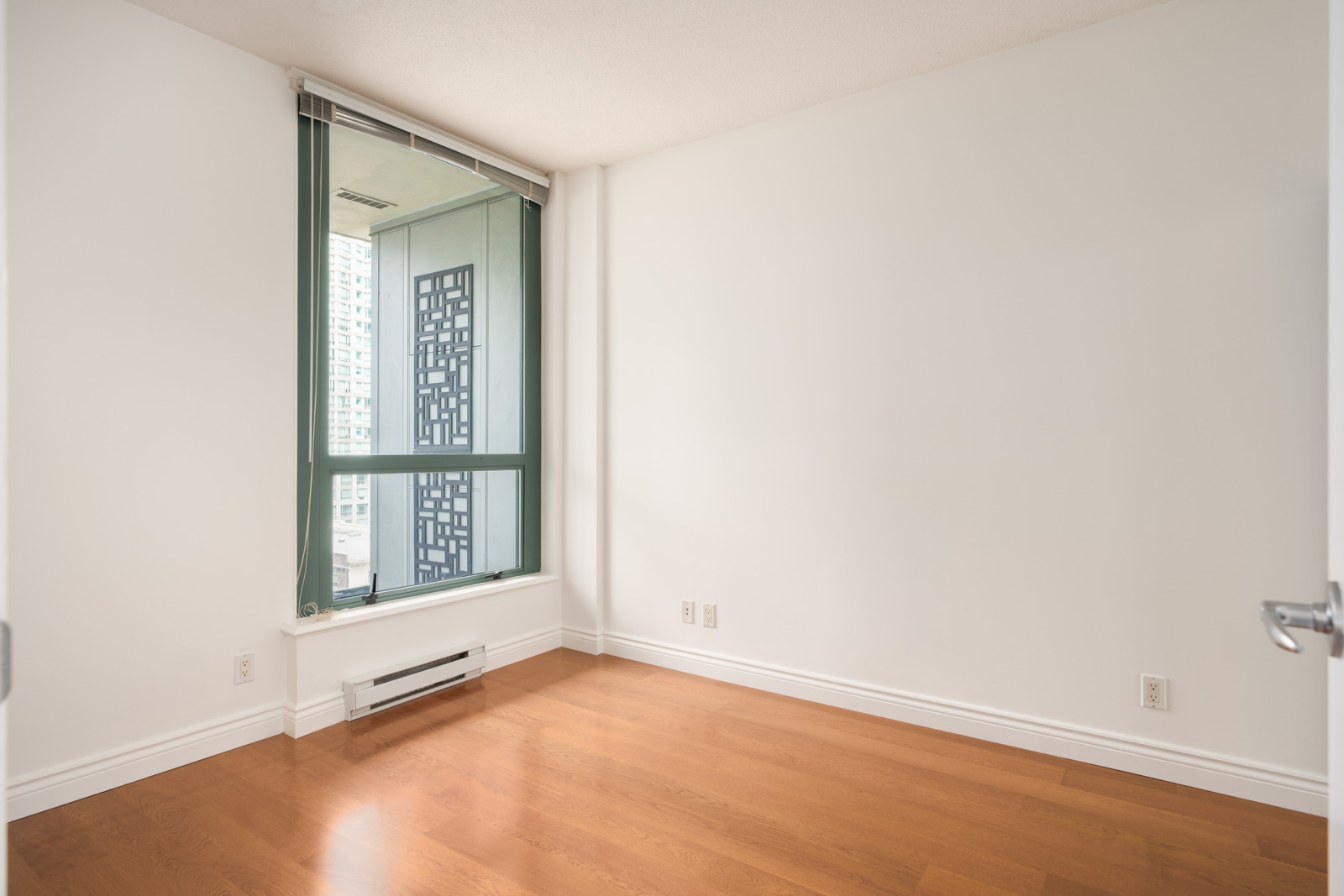 Unfurnished room at 1239 W Georgia St, Vancouver, featuring light walls, wood floors, a large window with city view, and baseboard heater.