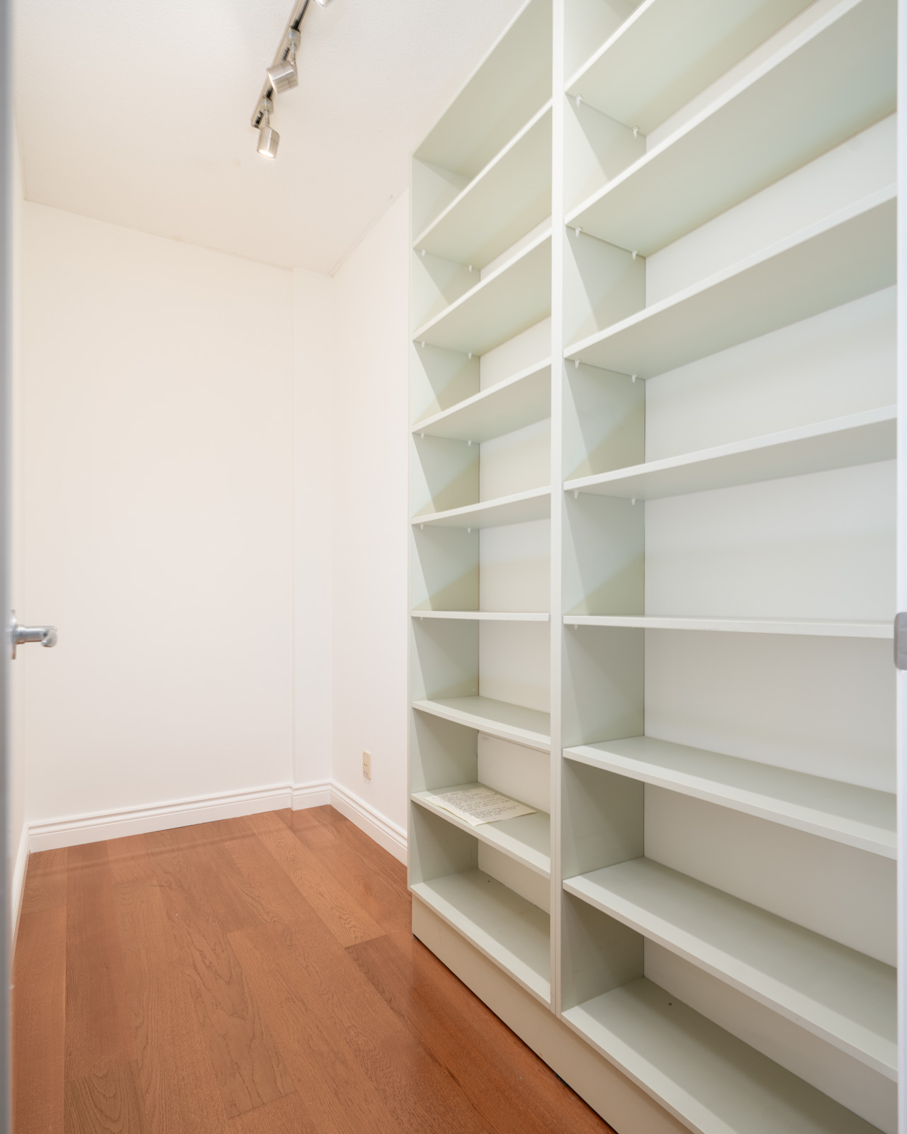 Empty walk-in closet with white built-in shelves, hardwood floor, and track lighting on 7th floor at 1239 W Georgia St, Vancouver.