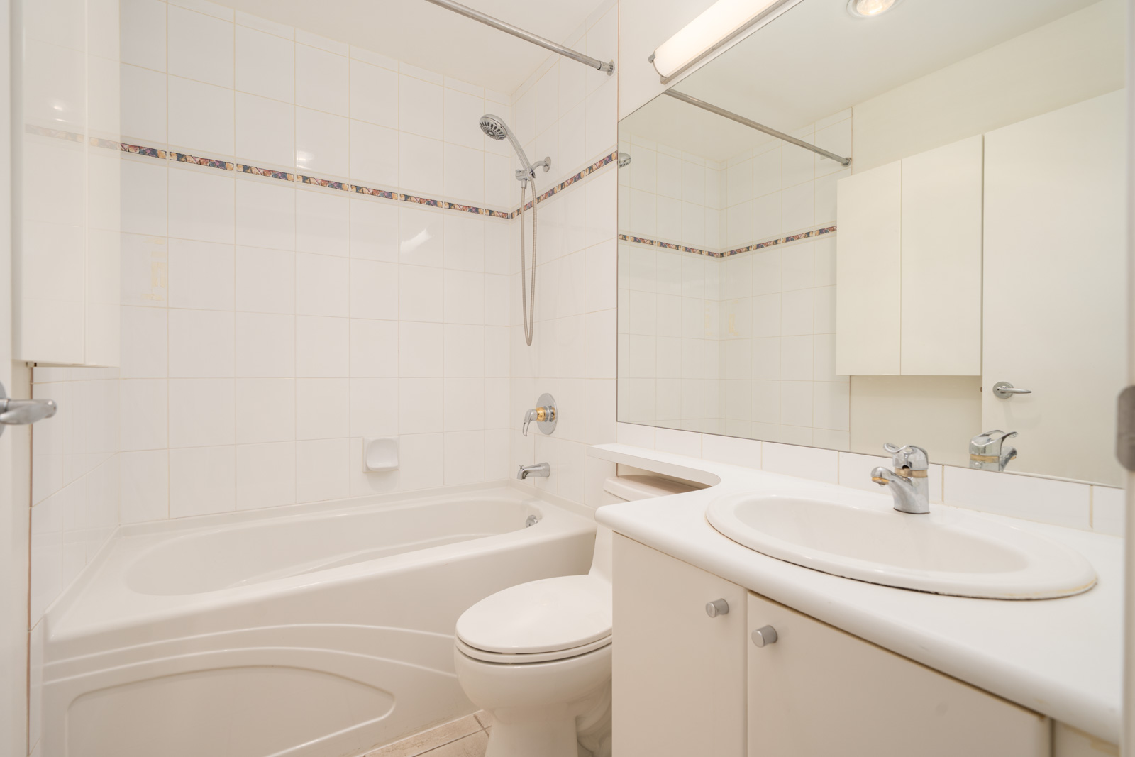 White bathroom, 7th Floor, 1239 W Georgia St, Vancouver: bathtub/shower combo, toilet, sink with counter, mirror, white tiled walls.