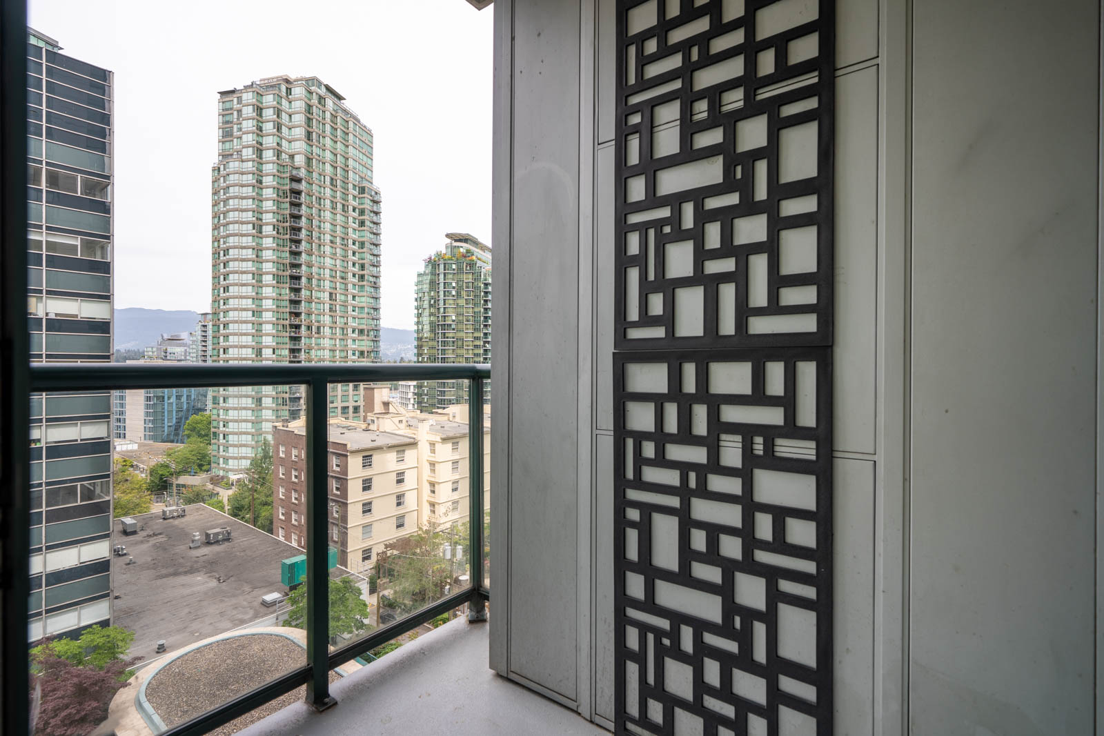 Seventh-floor balcony view at 1239 W Georgia St, Vancouver, with metal privacy screen, glass railing, and distant high-rises on a cloudy day.