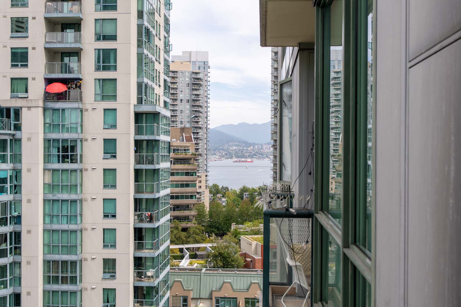 Seventh-floor balcony view at 1239 W Georgia St, Vancouver: high-rises, mountains, ship on water, green spaces below, cloudy sky.