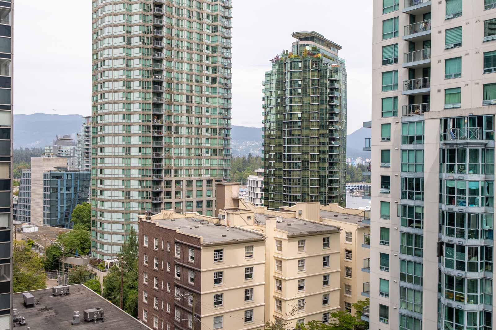 Vancouver skyline with high- and mid-rise apartments, including 1239 W Georgia St; mountains in the distance, overcast sky.