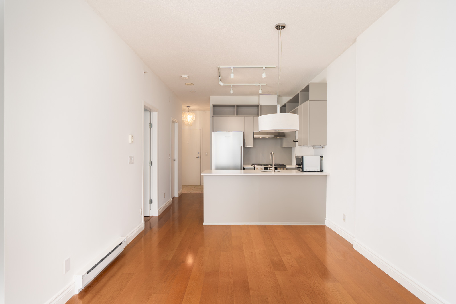 Modern, unfurnished kitchen at 1239 W Georgia St, Vancouver with white walls, wood floors, stainless appliances, and hallway view.