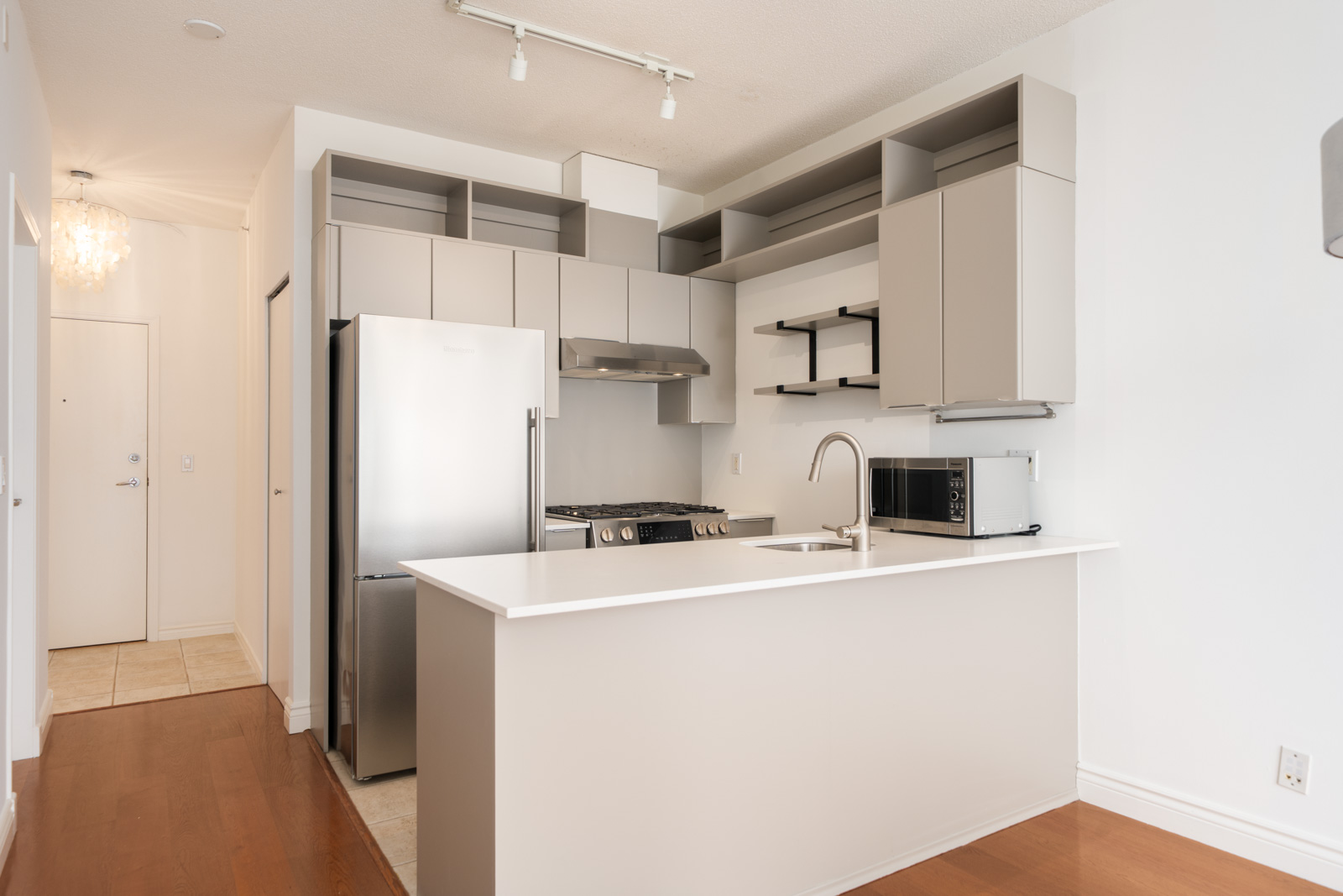 Modern kitchen with light gray cabinets, stainless steel appliances, open shelves, white island, hardwood floors; 7th Floor, Vancouver.