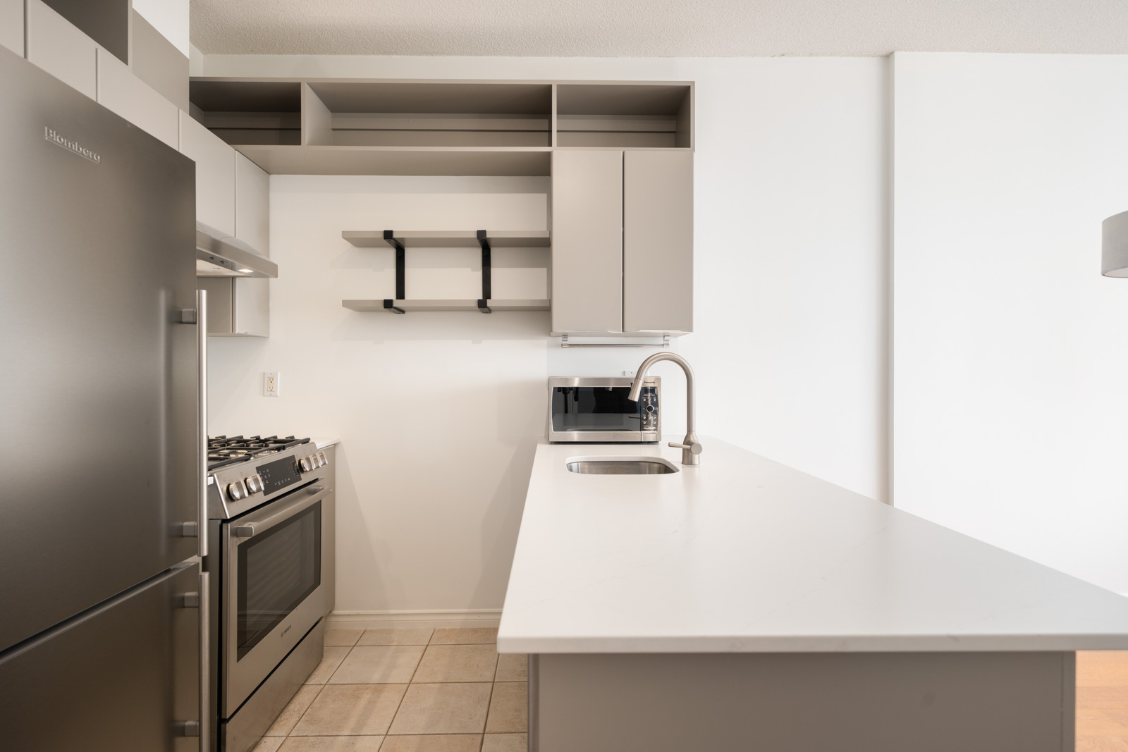 Modern kitchen on 7th floor at 1239 W Georgia St, Vancouver with stainless appliances, gray cabinets, open shelves, and white counters.