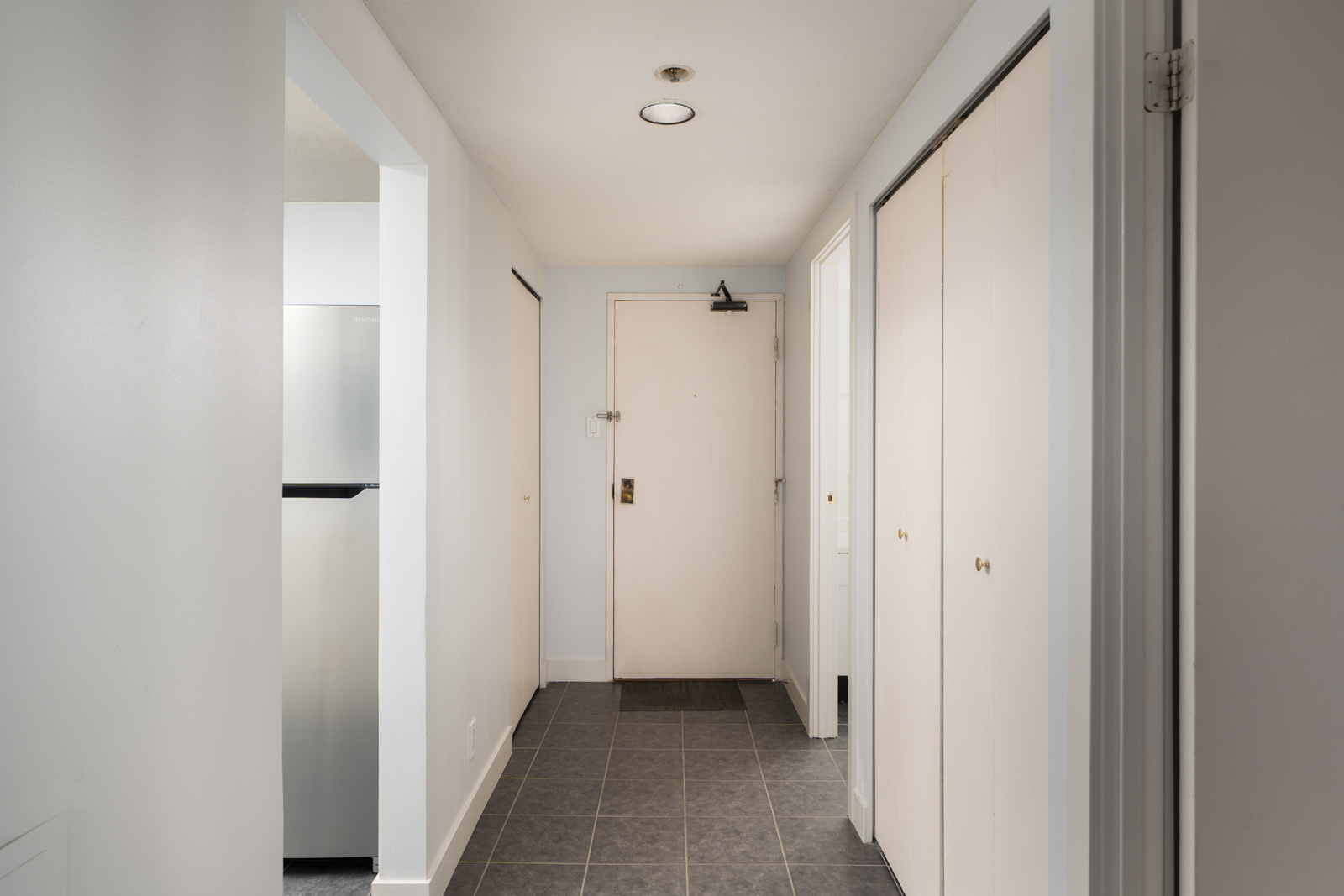 Hallway with gray tile floor, white walls, closed door at end, two cream closets on right, kitchen partly visible on left, Coquitlam.