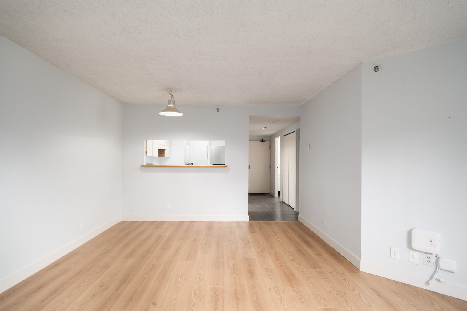 Empty 1st floor condo on Westview St, Coquitlam, with light wood floors, white walls, ceiling light, kitchen pass-through window.