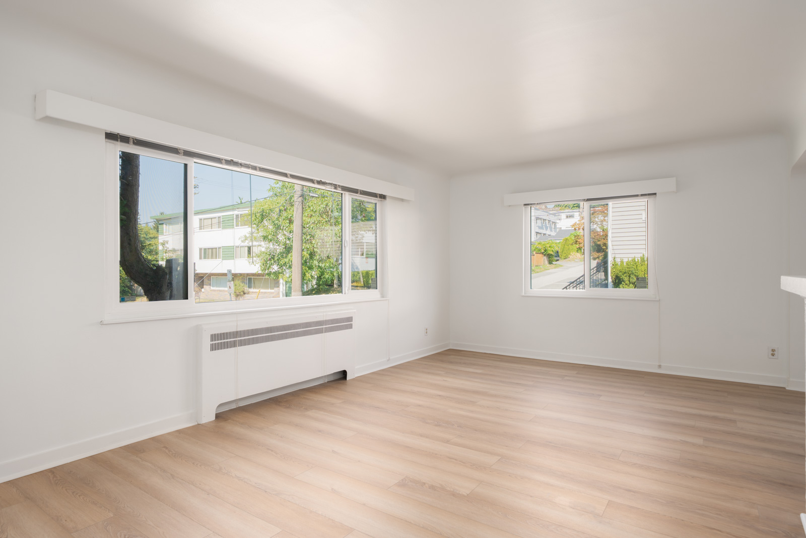 Unfurnished room with light wood floors, white walls, large windows, wall heater; 1st floor on Royal Avenue, New Westminster.