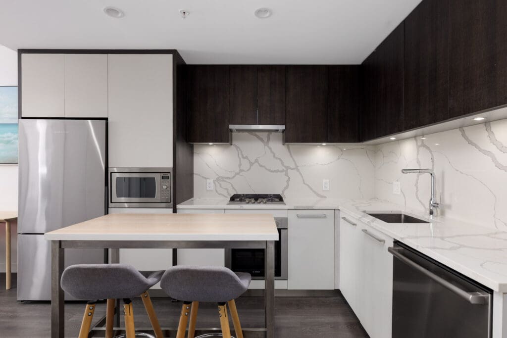Modern kitchen at 567 Clarke Rd, Coquitlam with dark uppers, white lowers, stainless appliances, marble backsplash, wood island, and two gray barstools.