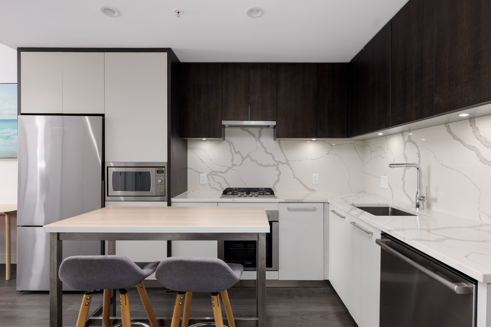 Modern kitchen at 567 Clarke Rd, Coquitlam with dark uppers, white lowers, stainless appliances, marble backsplash, wood island, and two gray barstools.