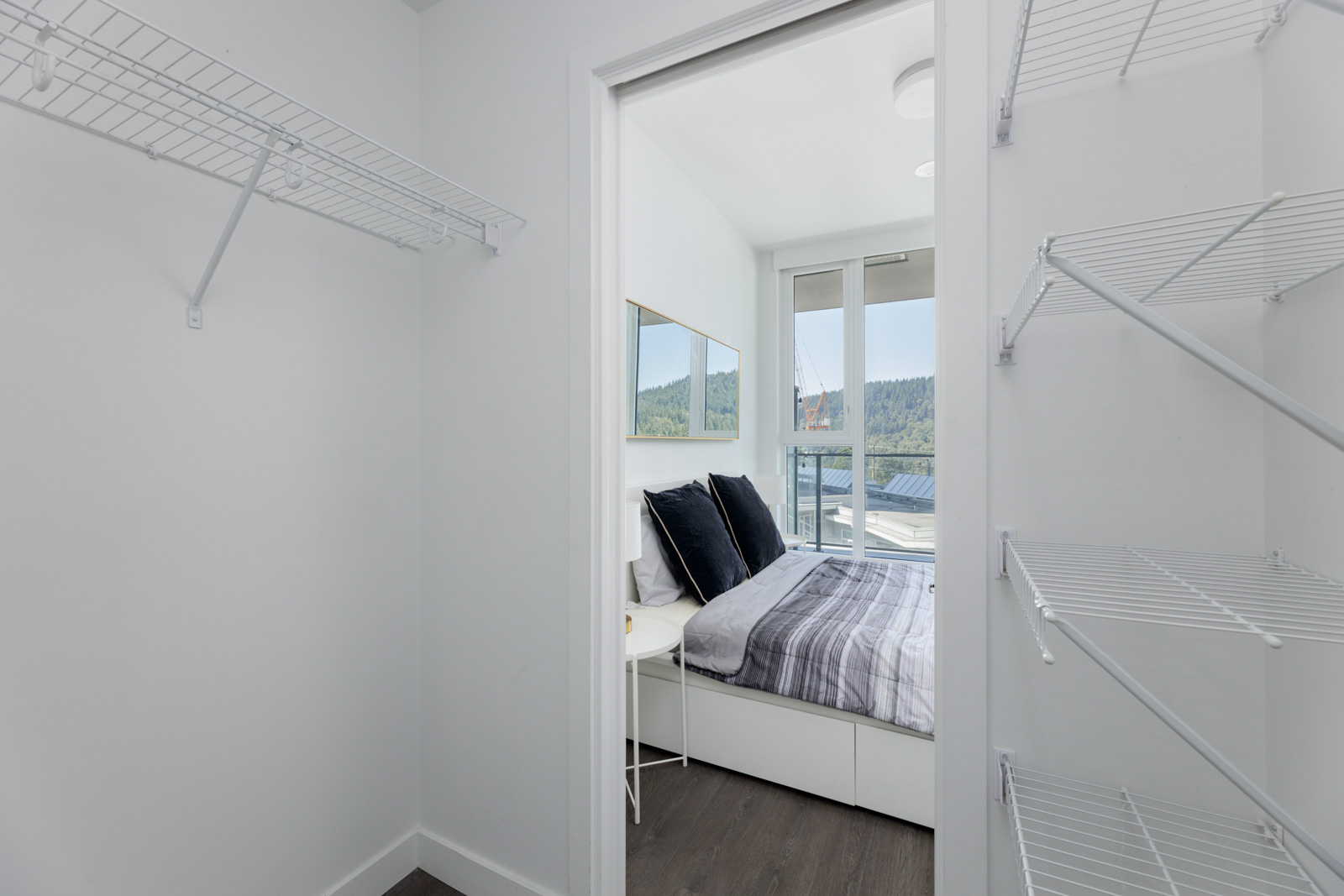 Walk-in closet with wire shelves opens to a bedroom at 567 Clarke Rd, Coquitlam, with bed and large windows overlooking outdoors.