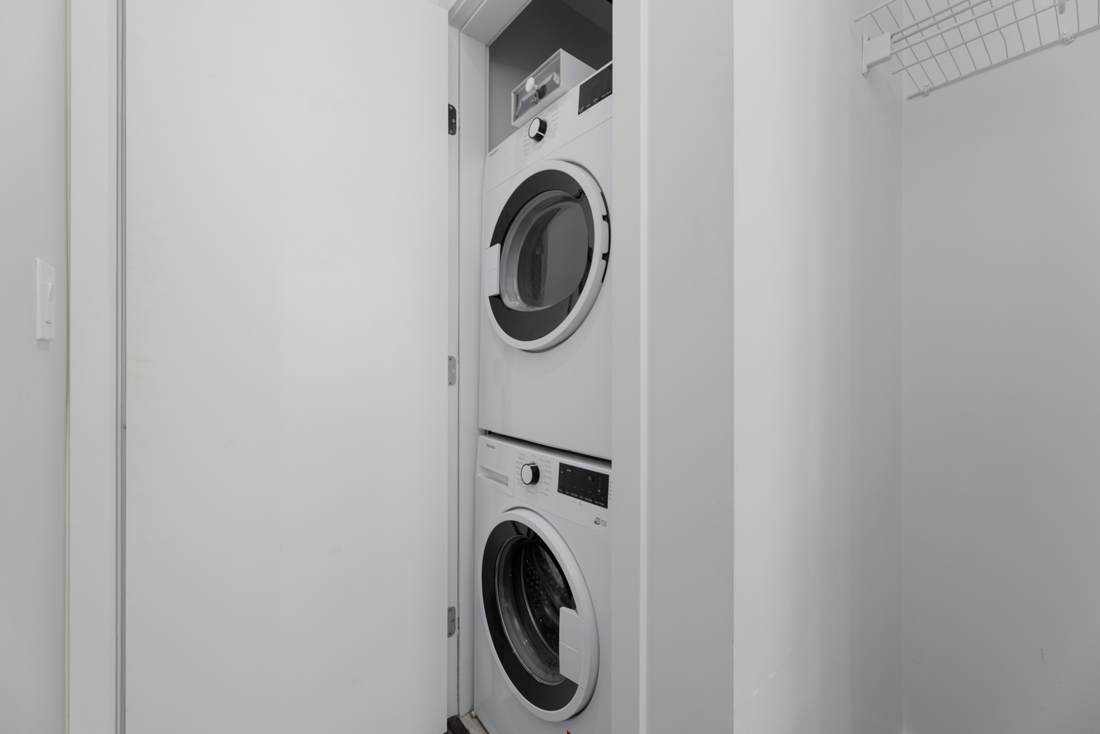 White stacked washer and dryer in a small laundry closet at 567 Clarke Rd, Coquitlam; open door and wire shelf on right.